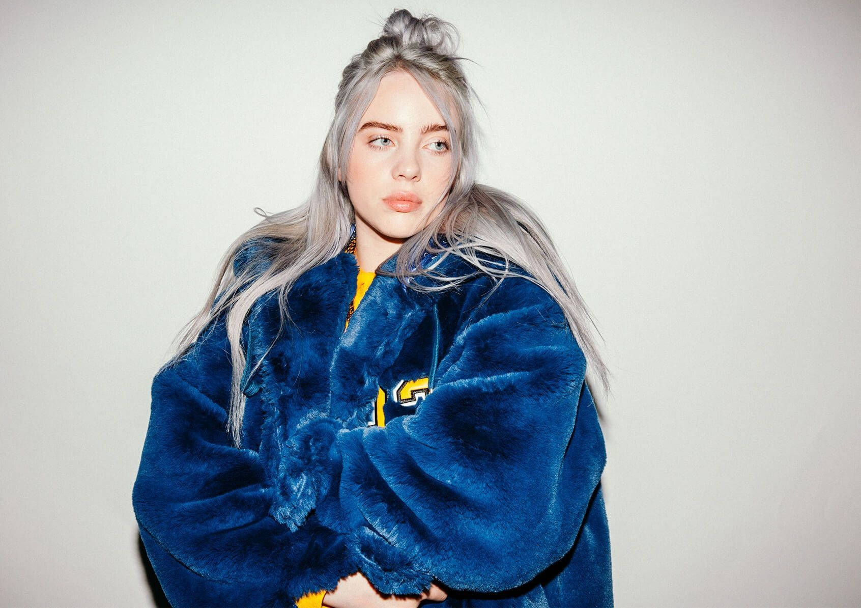 Billie Eilish 藍色絨毛毛衣美學壁紙 壁紙 — 一位銀髮年輕女性穿著毛絨藍色外套，背景為純白色。