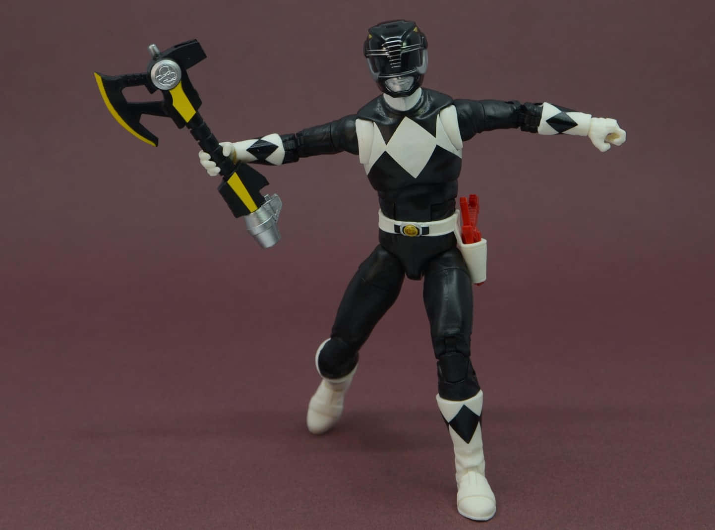  壁紙 — 一個黑白相間的Power Ranger動作人偶，手持一把黑色、黃色和銀色的斧頭，背景為純栗色。