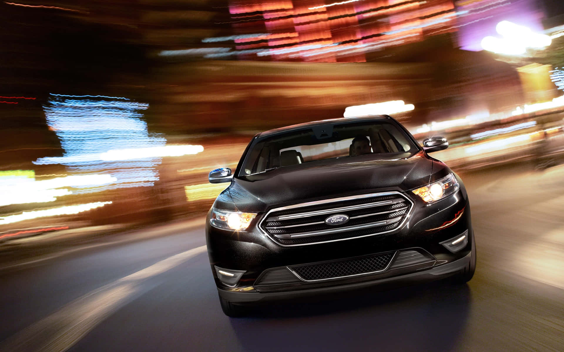 Ford Taurus 桌布 壁紙 — 一輛黑色福特 Taurus 在夜晚霓虹燈閃爍的城市中疾馳，背景中光線拖曳模糊。