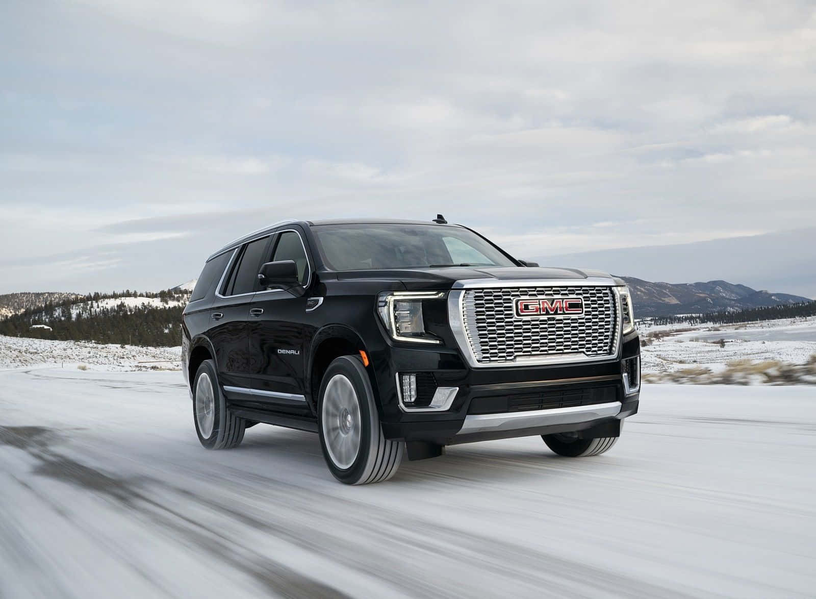 Gmc Yukon 桌布 壁紙 — 一輛黑色GMC Denali SUV在陰天之下，以模糊的動態穿越雪景。