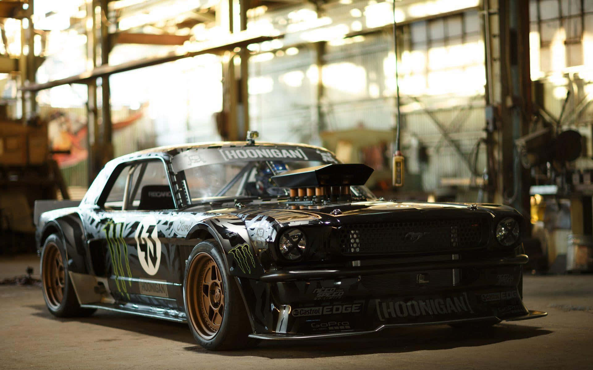Hoonigan 桌布 壁紙 — 一輛黑色Hoonigan Mustang飄移車配金色輪圈，停放在陽光照射的工業車庫內。