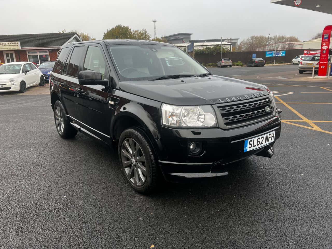 Land Rover Freelander 桌布 壁紙 — 一輛時尚的黑色Land Rover Freelander停泊在加油站，陰天潮濕的路面反射著灰色的天空。