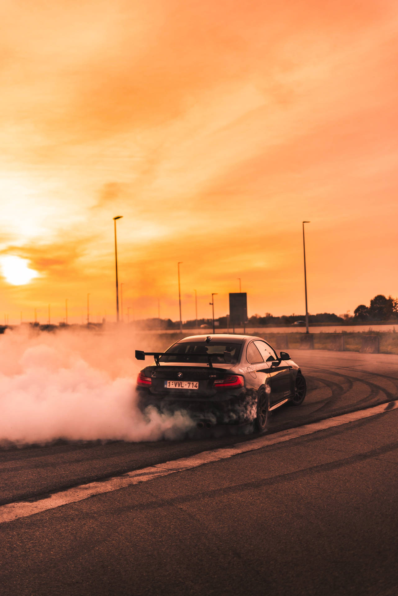 黑色跑車在夕陽下的空路上伴隨煙霧飄移。