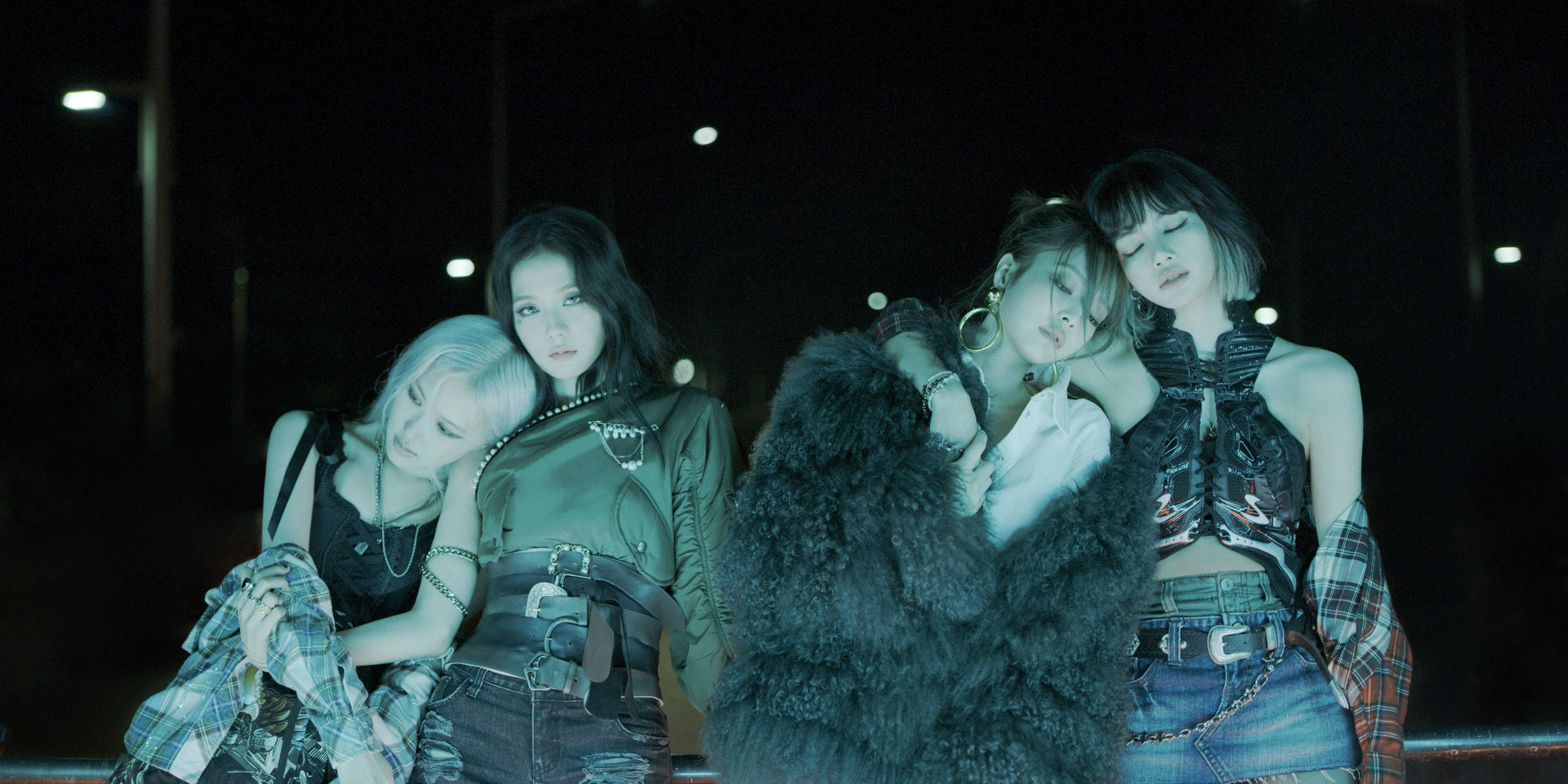 BLACKPINK 黑色服裝造型 壁紙 — 四位時尚女性穿著前衛服裝，在夜晚的霓虹燈下緊密擺姿勢，帶有憂鬱的藍綠色調。