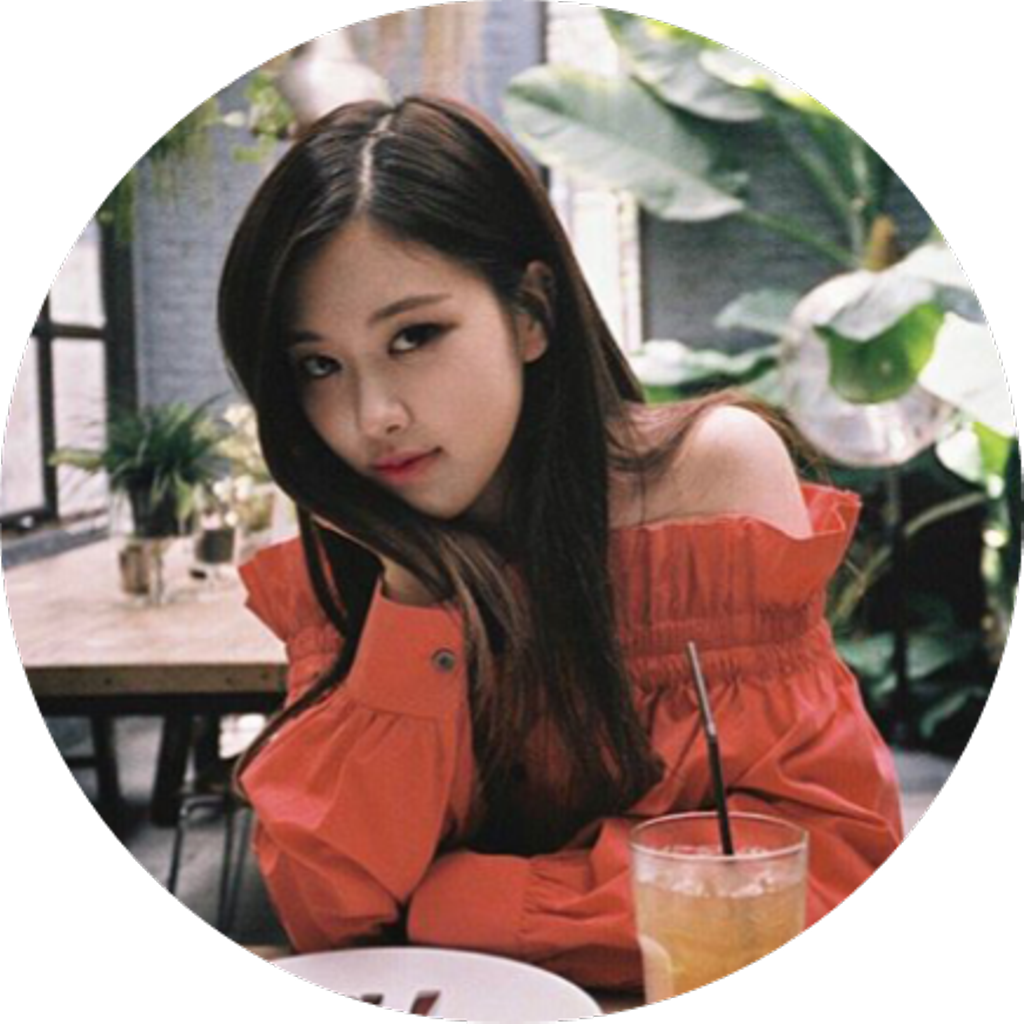 BLACKPINK成員咖啡廳造訪 壁紙 — 一位年輕女性身穿鮮豔的橙色露肩上衣，坐在咖啡廳的桌子旁，手持飲品，若有所思地凝視著鏡頭。