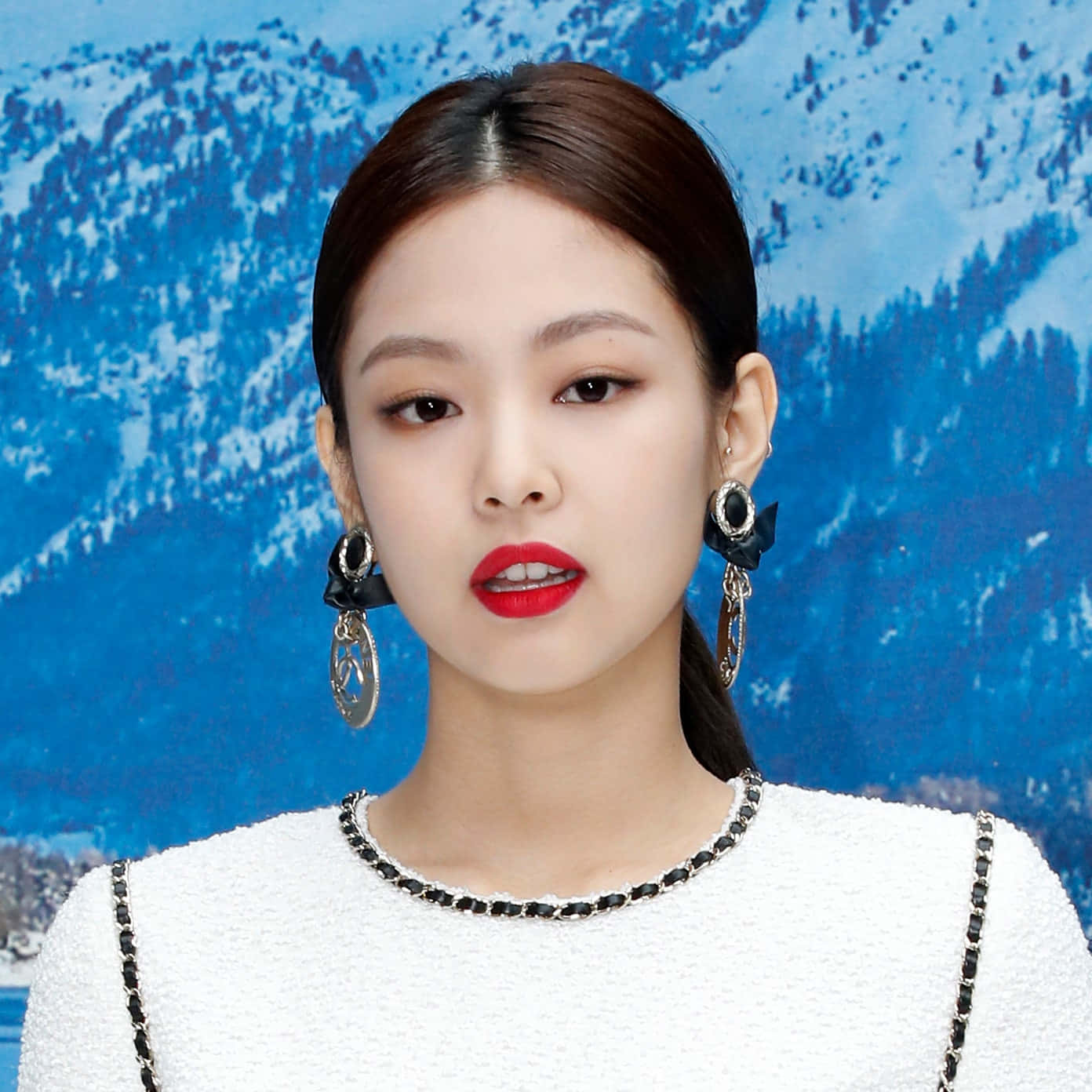 BLACKPINK Jennie Kim街頭風格造型照 壁紙 — 一位優雅嘅女士，塗上大膽嘅紅唇，戴住搶眼嘅耳環，企喺白雪覆蓋嘅山景前面。
