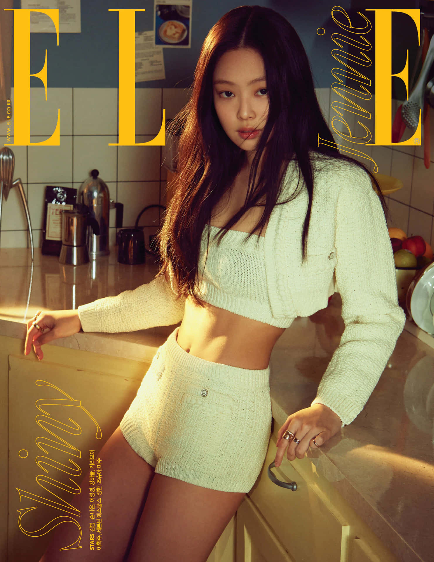BLACKPINK Jennie為《Elle》雜誌拍攝廚房造型照 壁紙 — Jennie 自信地擺姿勢，身穿奶油色針織套裝，背景是溫暖的廚房，帶有金色燈光。