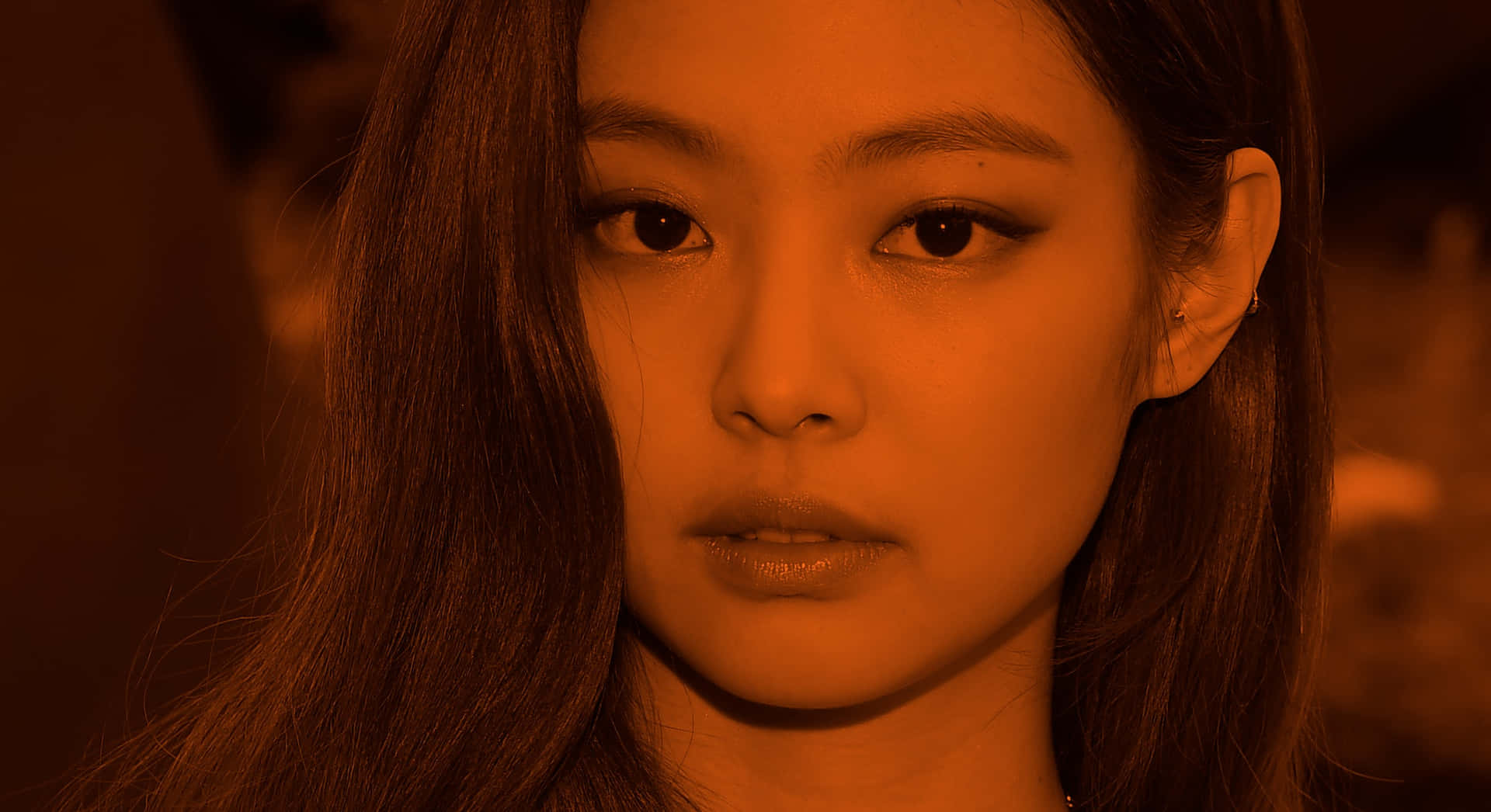 BLACKPINK Jennie Kim紅色濾鏡頭像照 壁紙 — 一位長髮深色女子的特寫肖像，在溫暖的橙色燈光下，她專注的目光直視前方。