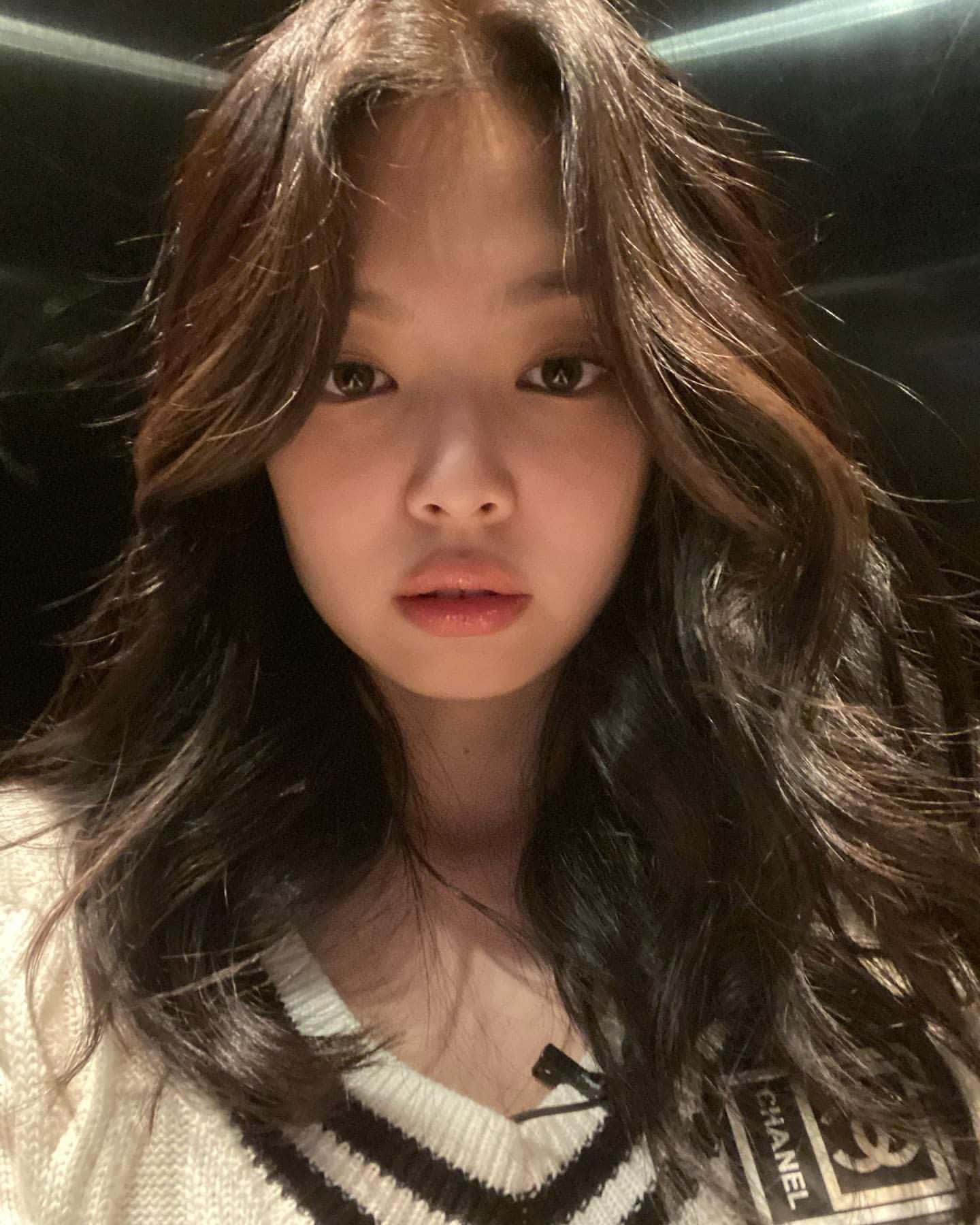 BLACKPINK Jennie 自拍照片 壁紙 — 一位年輕女性的特寫肖像，她擁有長長的深色波浪髮，穿著黑白條紋毛衣，背景為深色。