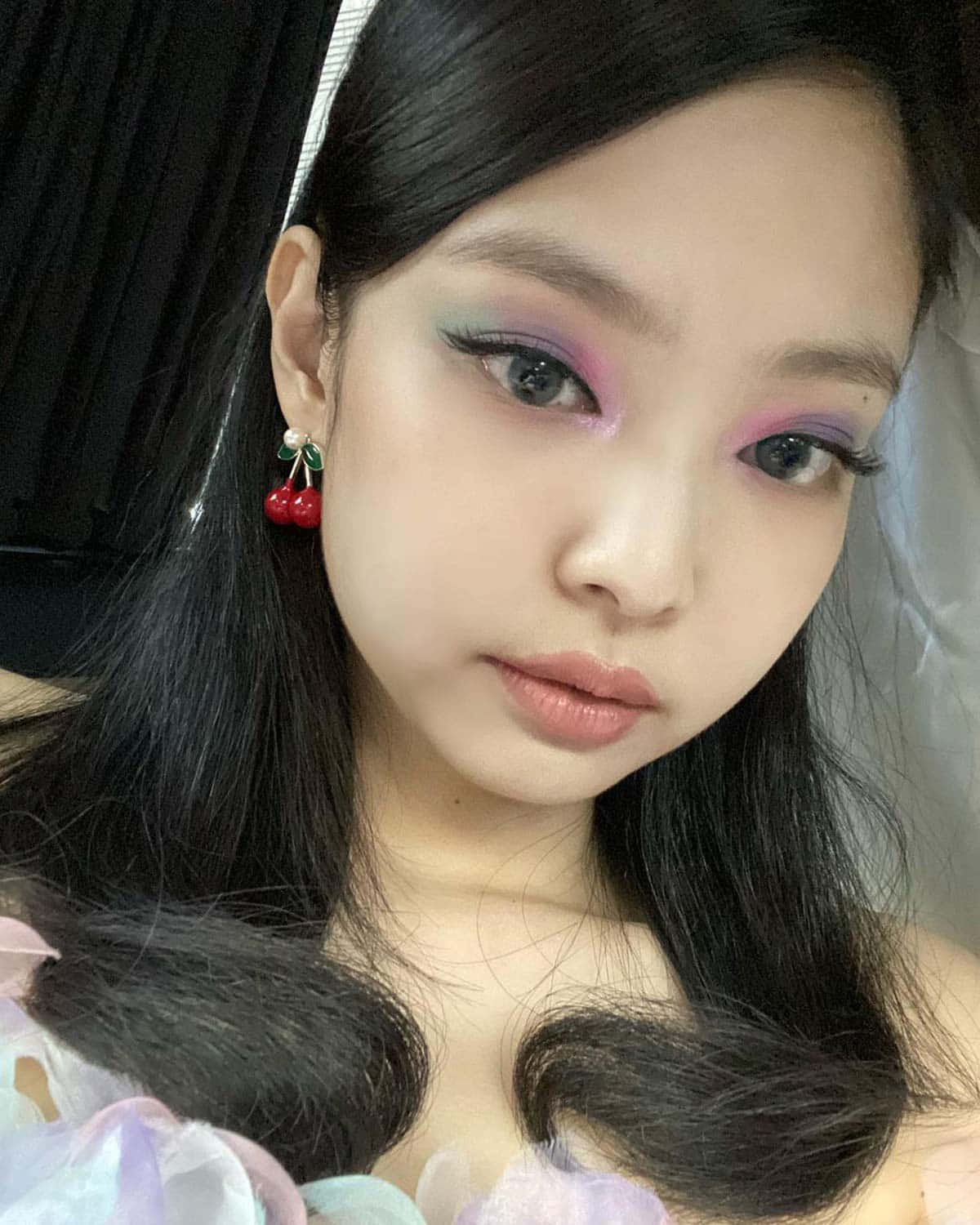 BLACKPINK Jennie Kim化妝精緻自拍照 壁紙 — 一個女人嘅特寫肖像，佢化咗大膽嘅粉彩眼影，戴住櫻桃耳環，背景係深色窗簾。