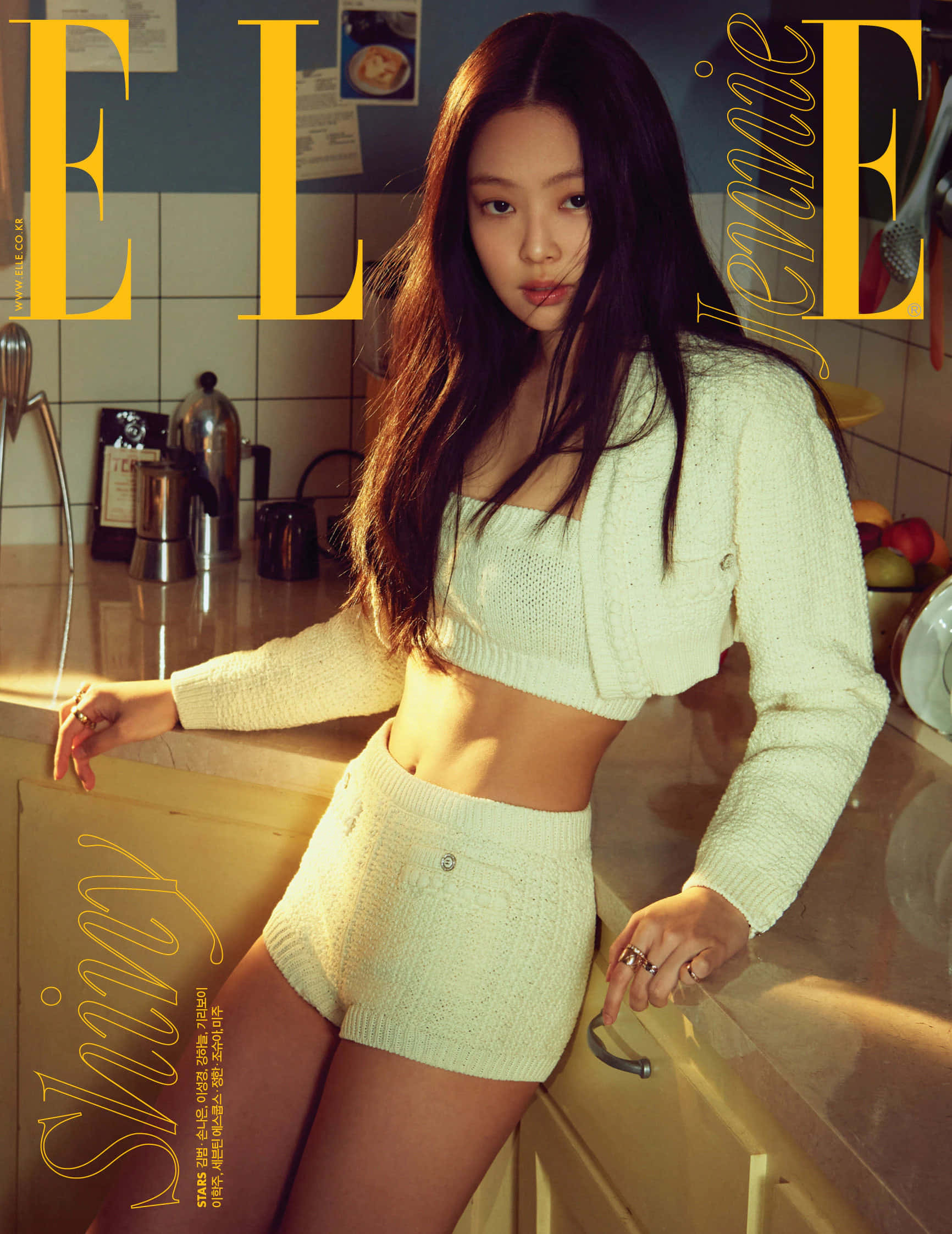 BLACKPINK Jennie為《Elle》雜誌拍攝廚房造型照 壁紙 — Jennie 自信地擺姿勢，身穿奶油色針織套裝，背景是溫暖的廚房，帶有金色燈光。