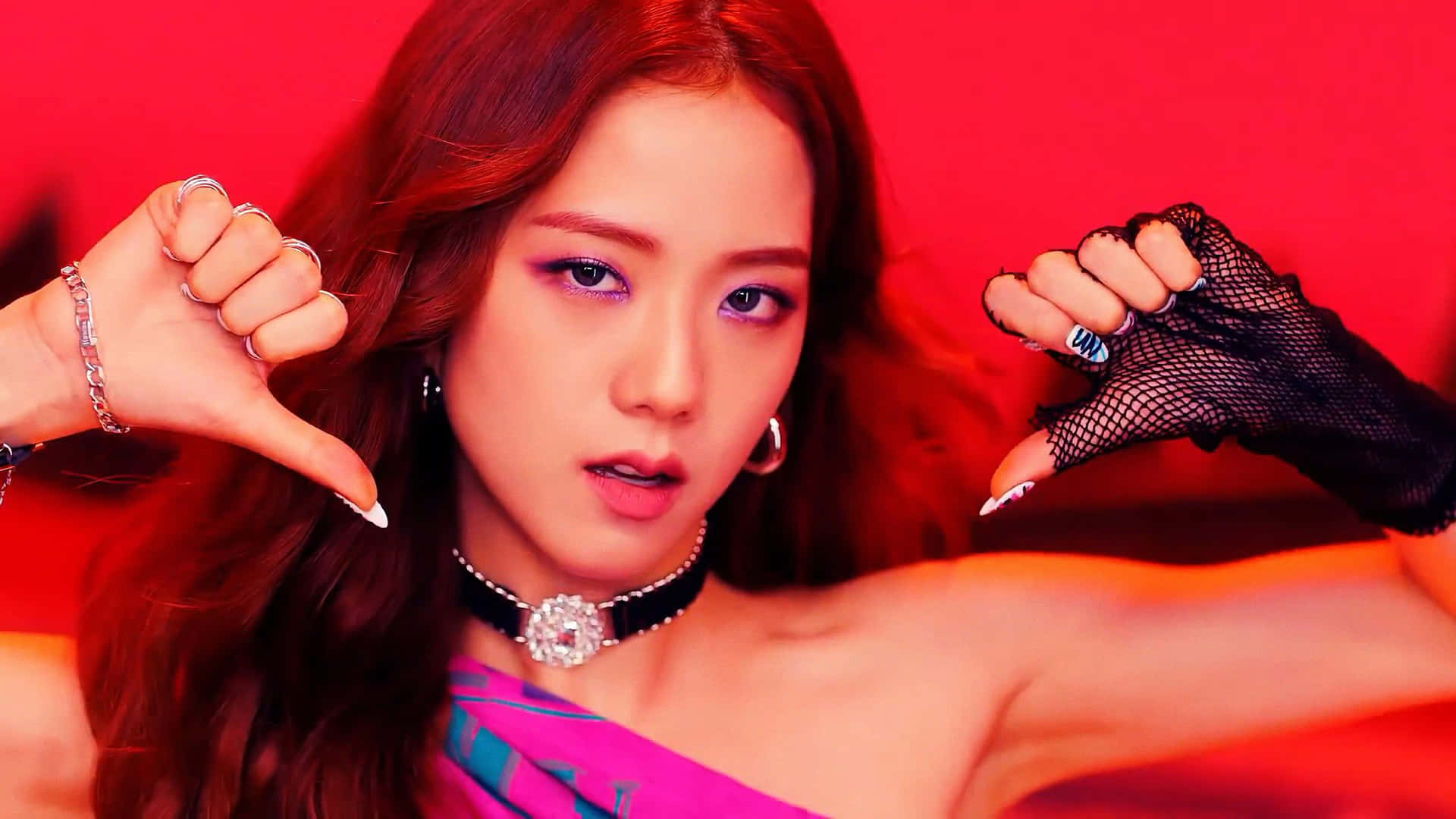 BLACKPINK Jisoo 激情心碎手勢 壁紙 — 一位魅力四射的紅髮女性，化著大膽的妝容，在鮮紅色的背景下做出拇指向下的手勢。
