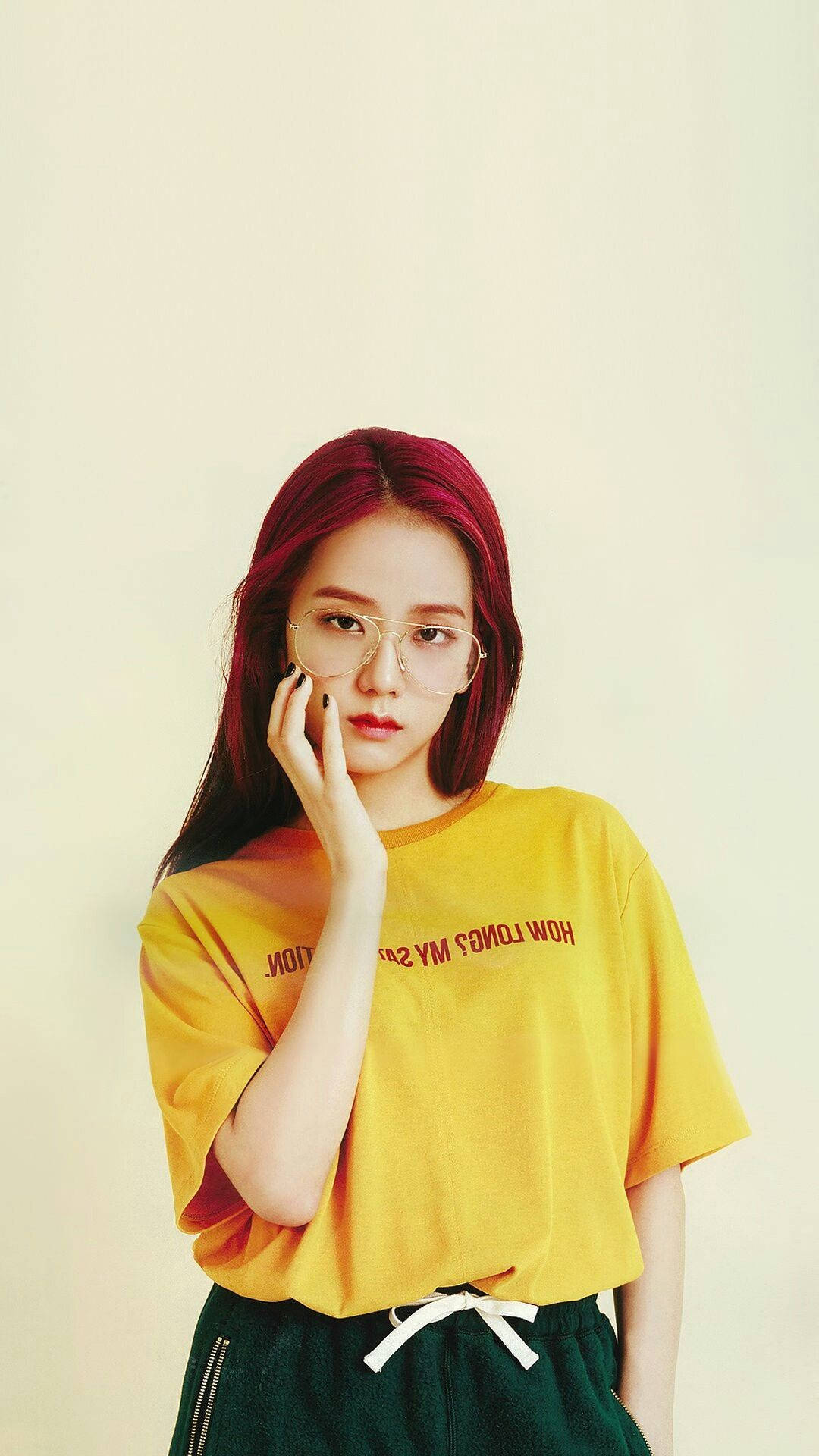 BLACKPINK Jisoo 戴眼鏡穿黃色上衣，活力四射 壁紙 — 一位年輕女性，擁有鮮豔的紅髮和眼鏡，穿著黃色T恤，在純米色背景前若有所思地擺姿勢。