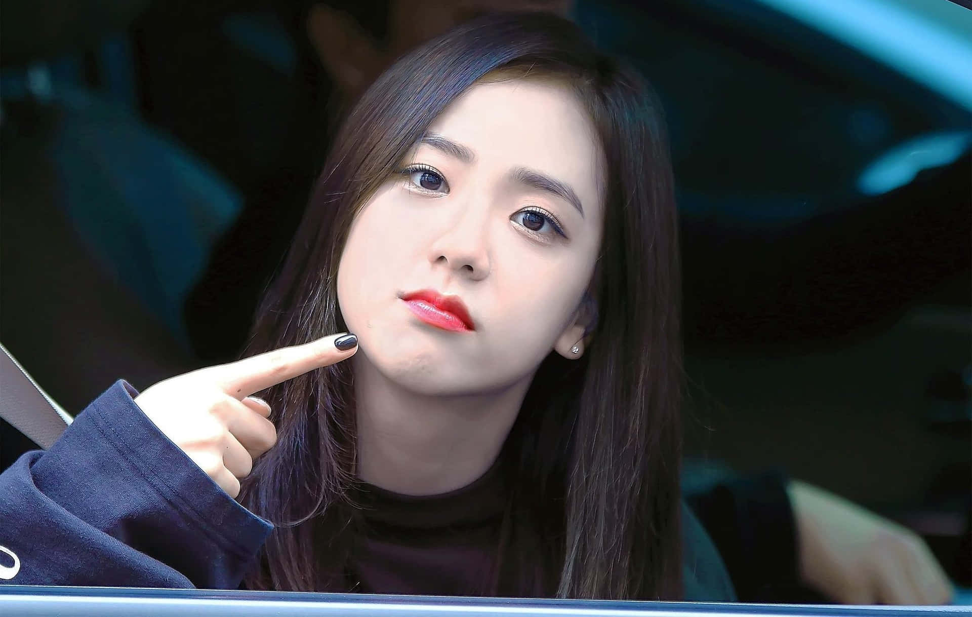 BLACKPINK Jisoo 車內愛心表情 壁紙 — 一位深色頭髮、紅唇的年輕女子晚上坐在車內，指著自己的臉頰。