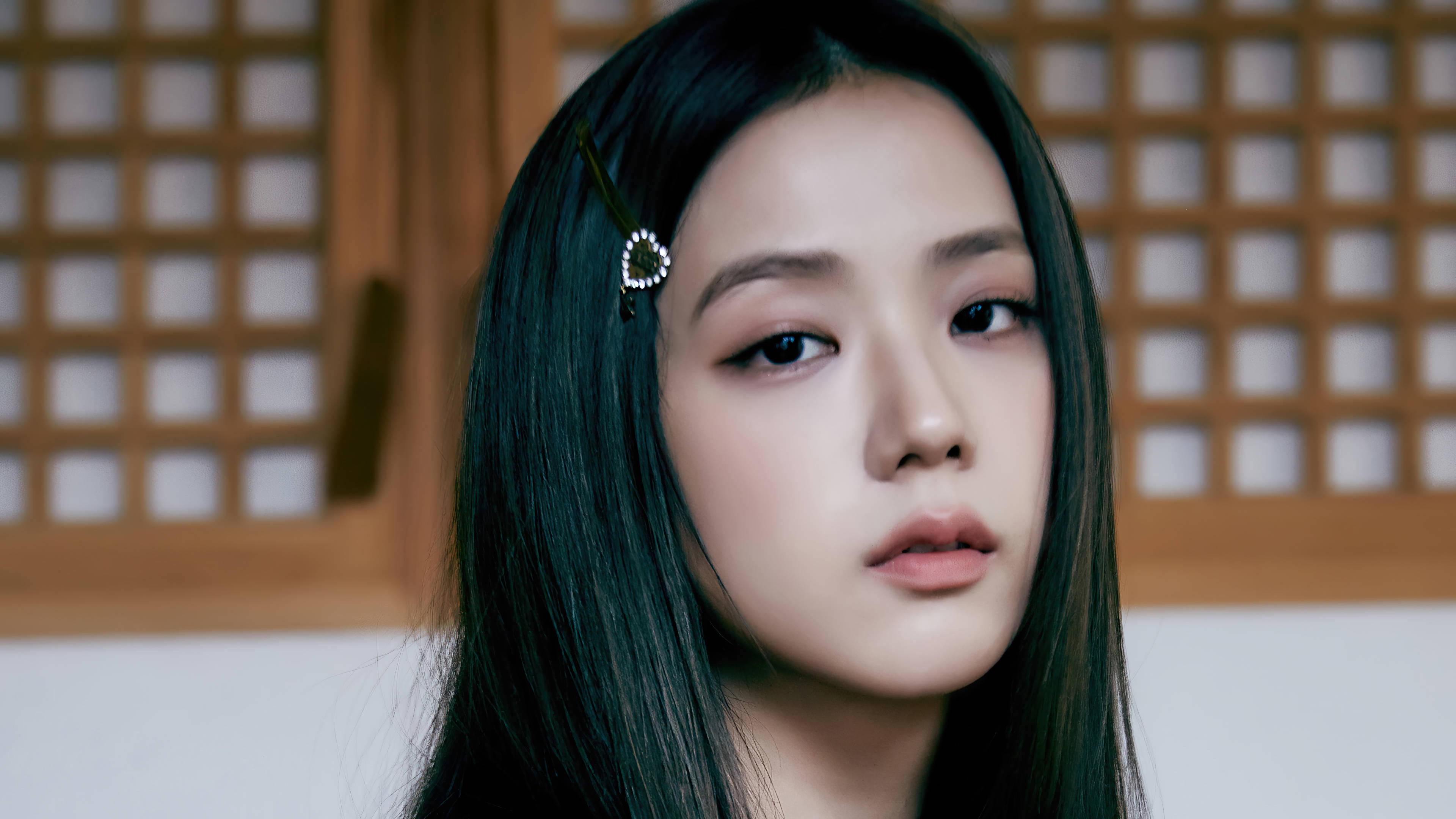 Blackpink Jisoo夏日 壁紙 — 一位長黑髮、戴珍珠髮夾的年輕女子，在木格柵背景前溫柔凝視。