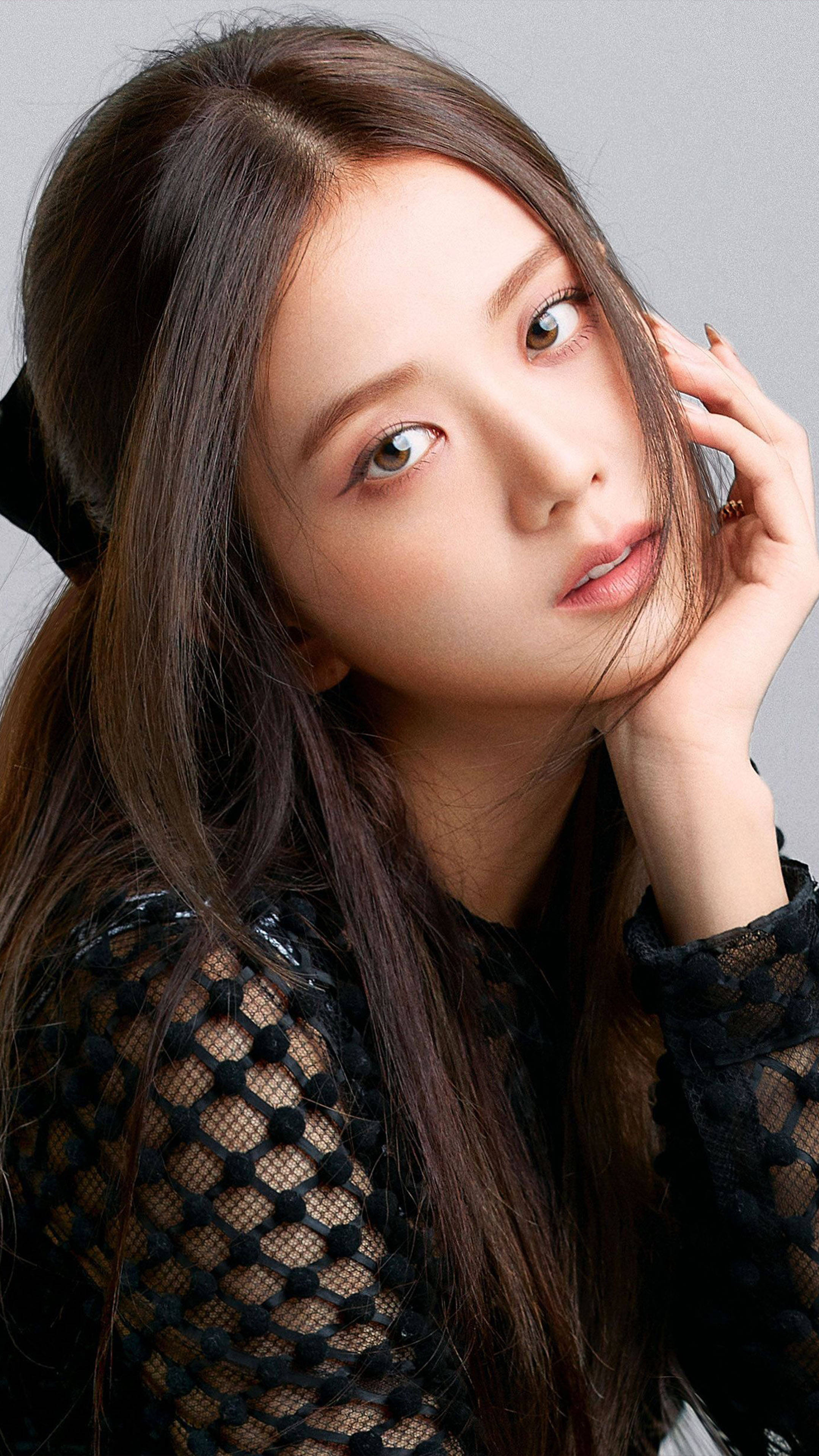 Blackpink Jisoo專屬肖像 壁紙 — 一位年輕女性，長長嘅棕色頭髮，穿著黑色網眼上衣，喺中性灰色背景前，將下巴擱喺手上，溫柔咁凝視。