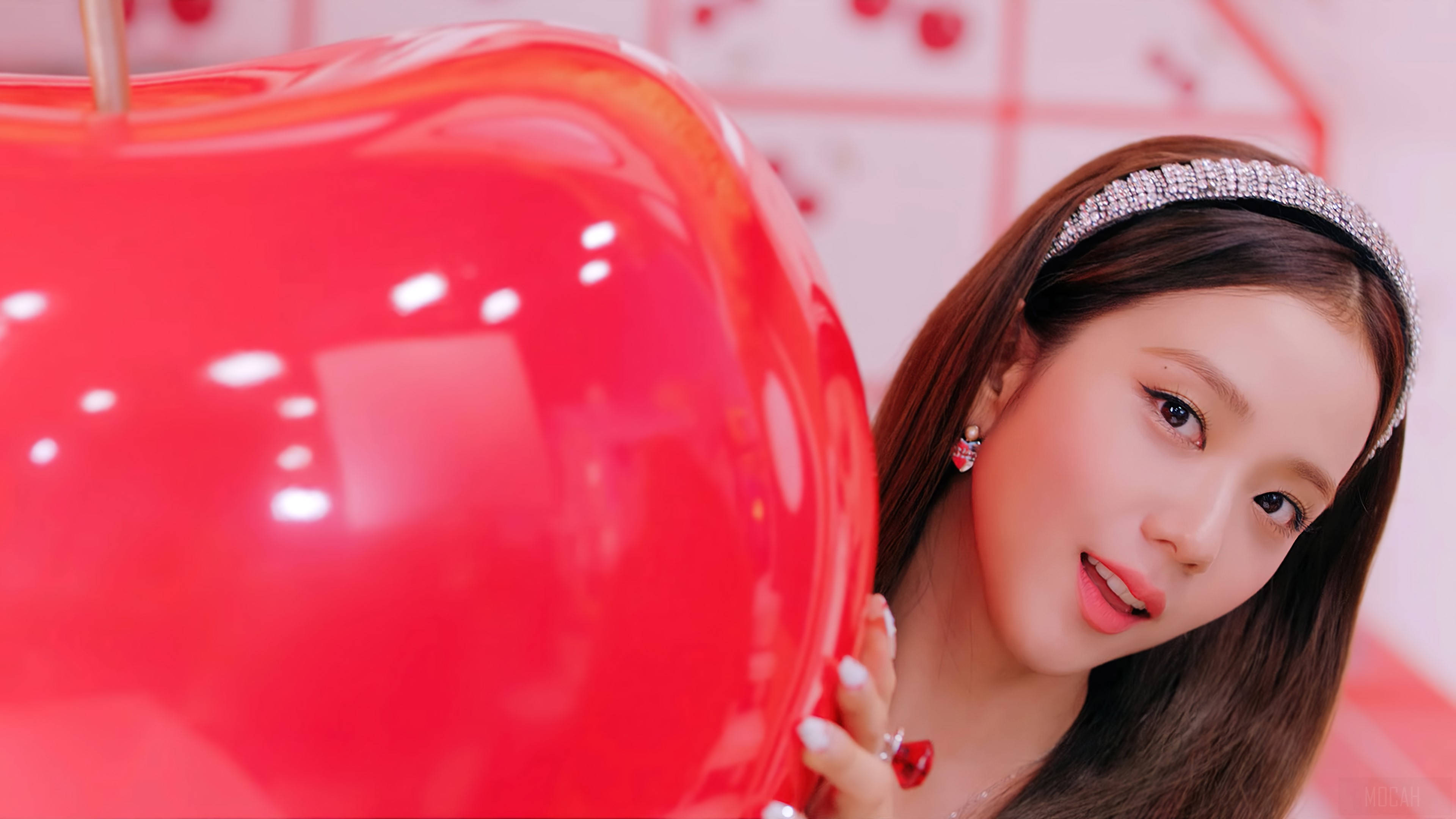 Blackpink Jisoo櫻花 壁紙 — 一位戴著寶石頭帶的年輕女子在明亮的粉紅色房間裡，從一個巨大的光澤紅蘋果後面頑皮地探出頭來。