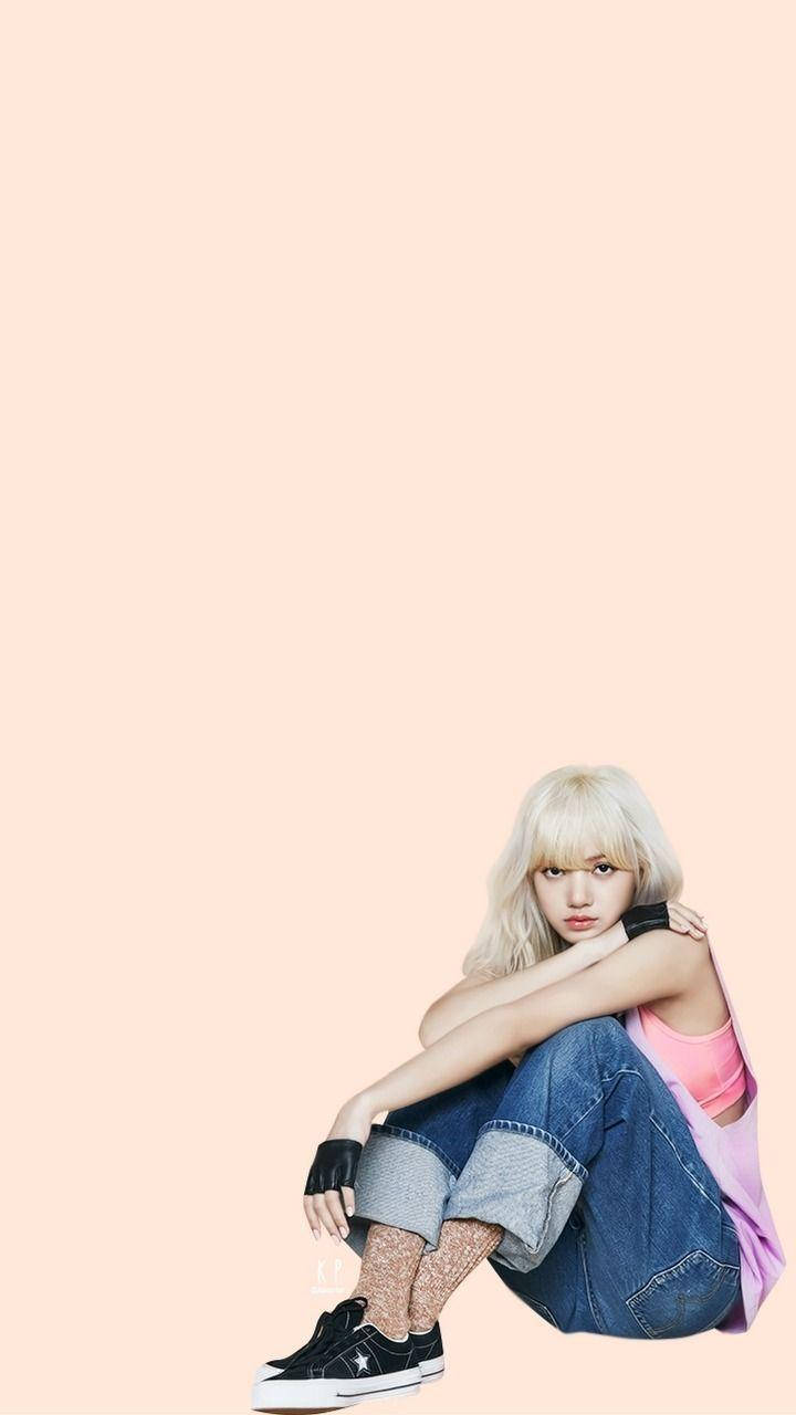 BLACKPINK LISA 坐姿 壁紙 — 一位金髮年輕女性盤腿坐在純色蜜桃色背景前，穿著牛仔褲和黑色運動鞋。