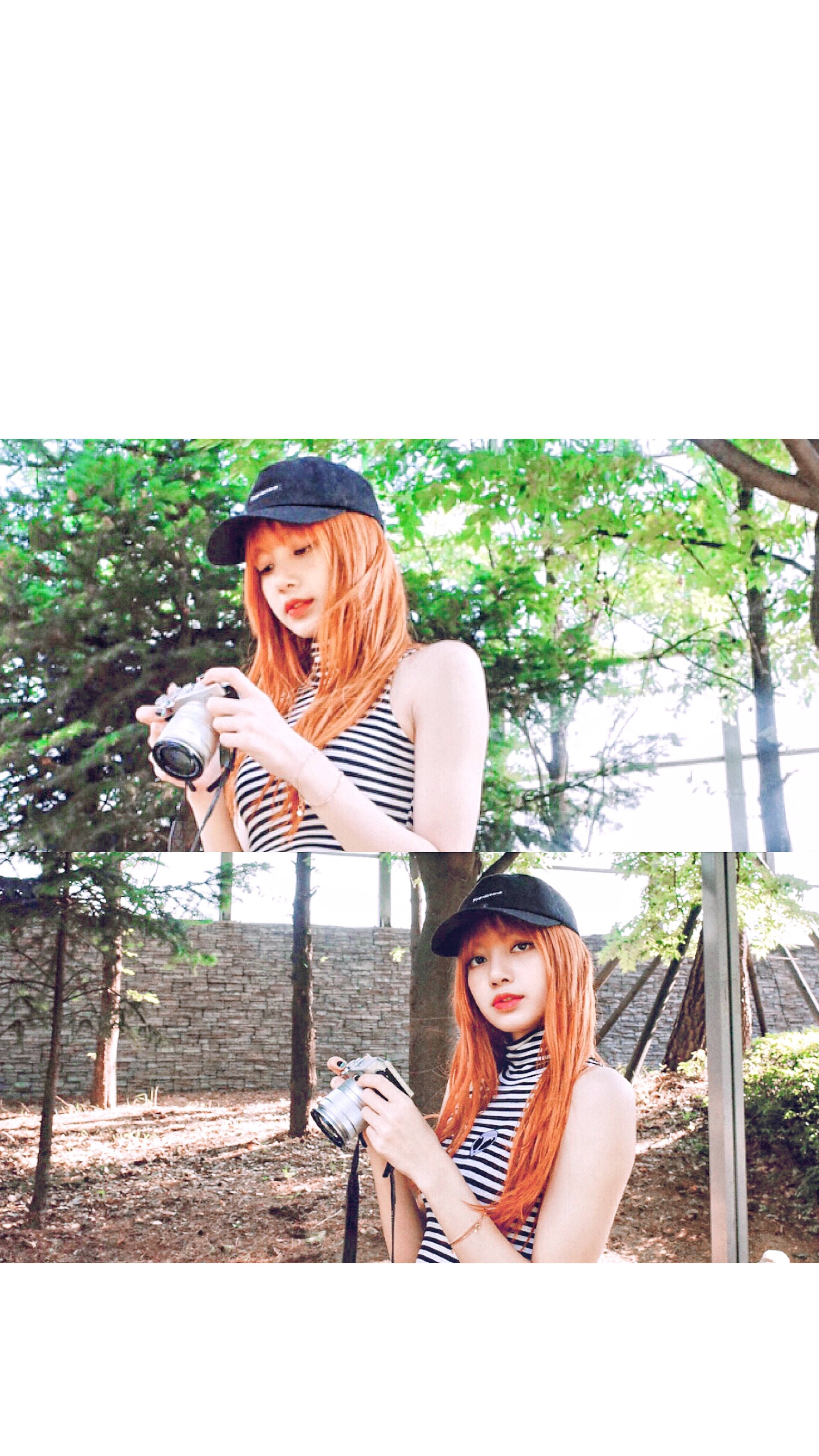 BLACKPINK LISA 持相機 壁紙 — 一位年輕女性，擁有鮮豔的橙色頭髮和黑色帽子，在陽光明媚的樹林地區手持相機。