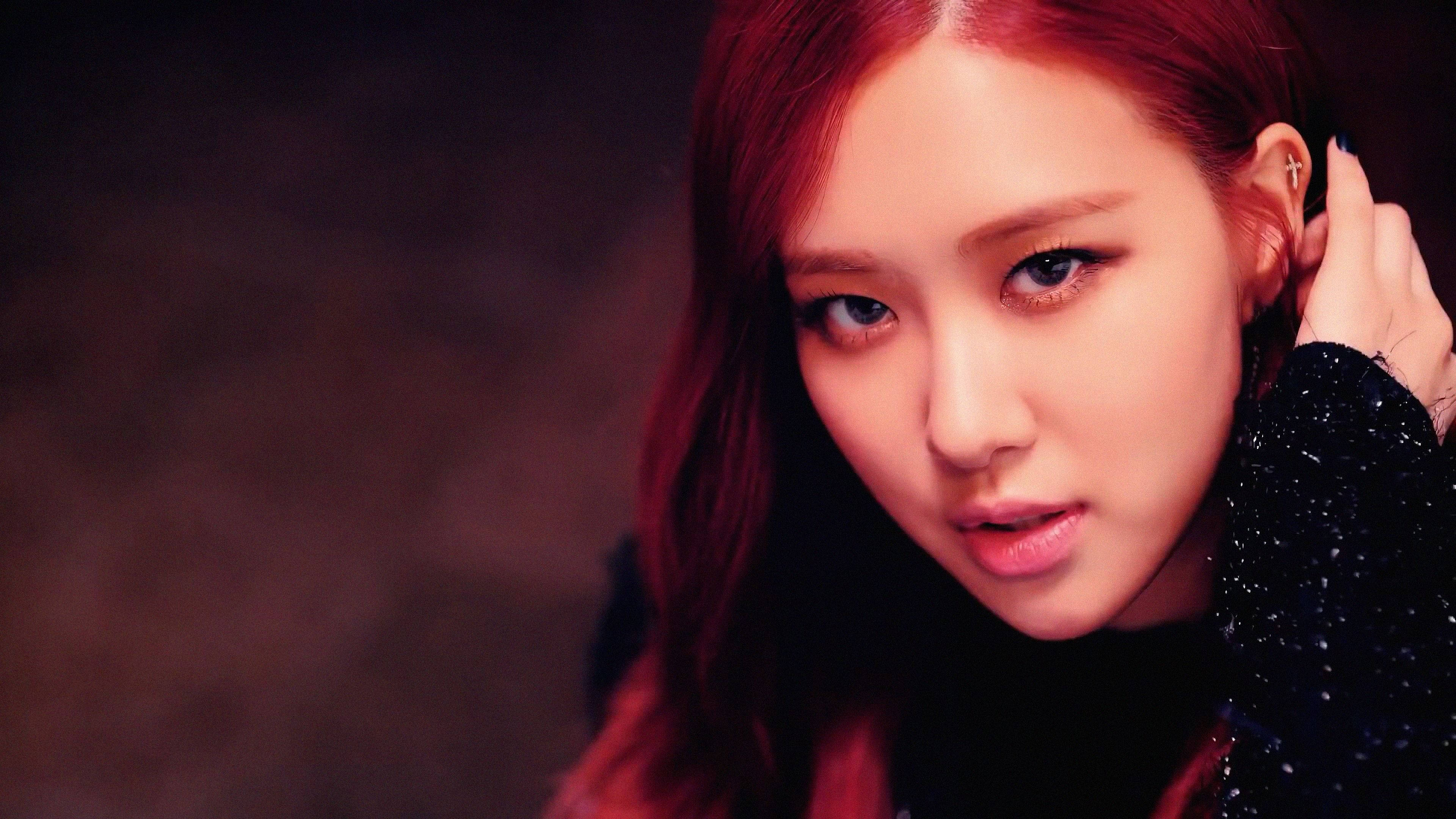 BLACKPINK 明星成員 壁紙 — 一位擁有鮮豔紅髮和強烈眼神的女性的特寫肖像，穿著黑色閃亮上衣，背景陰暗有氣氛。