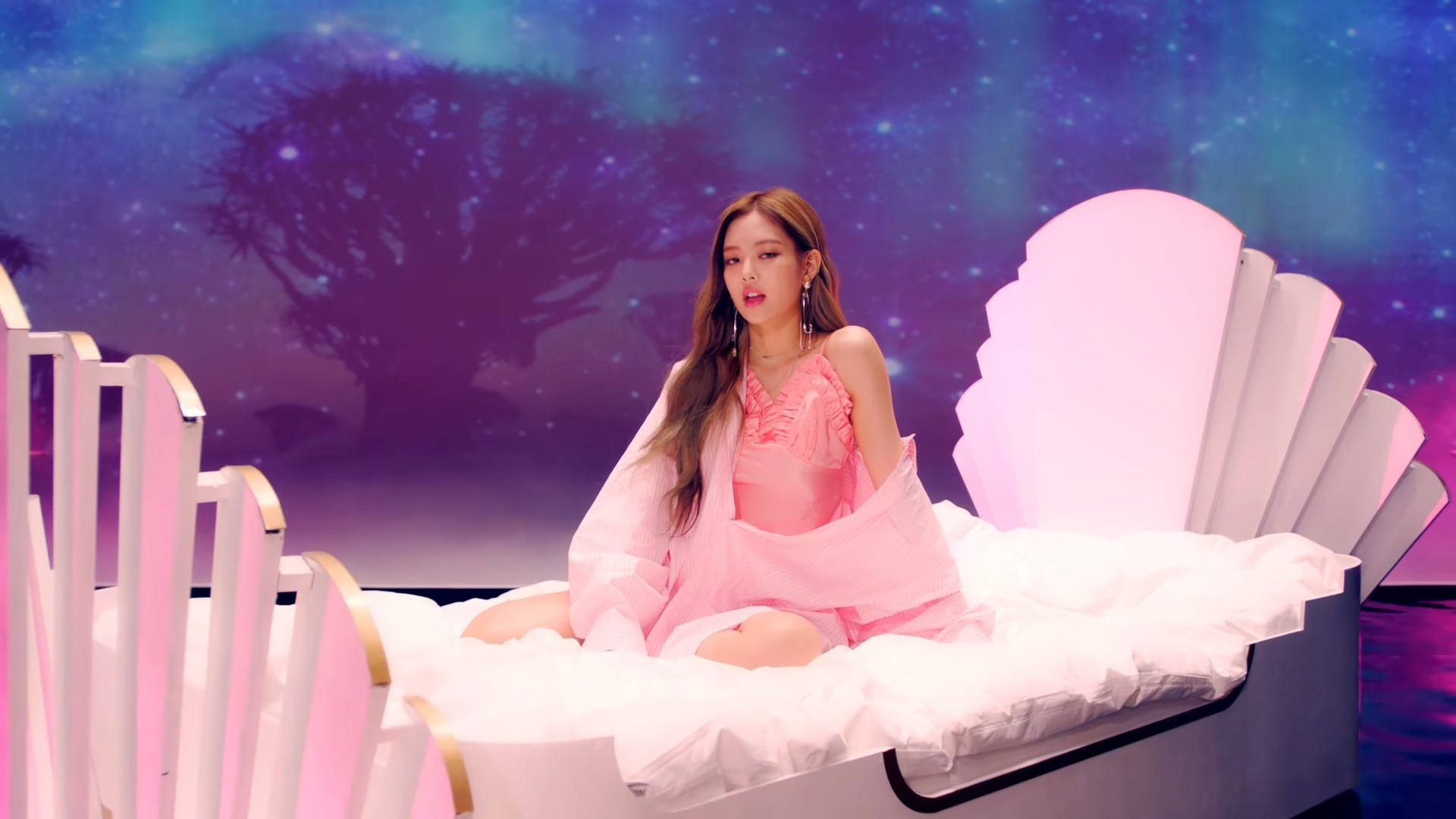BLACKPINK Jennie出演《As If It's Your Last》MV 壁紙 — 一位身穿粉紅色衣服的女性坐在白色貝殼形床上，背景是繁星點點的紫色和藍色宇宙，有一棵剪影樹。