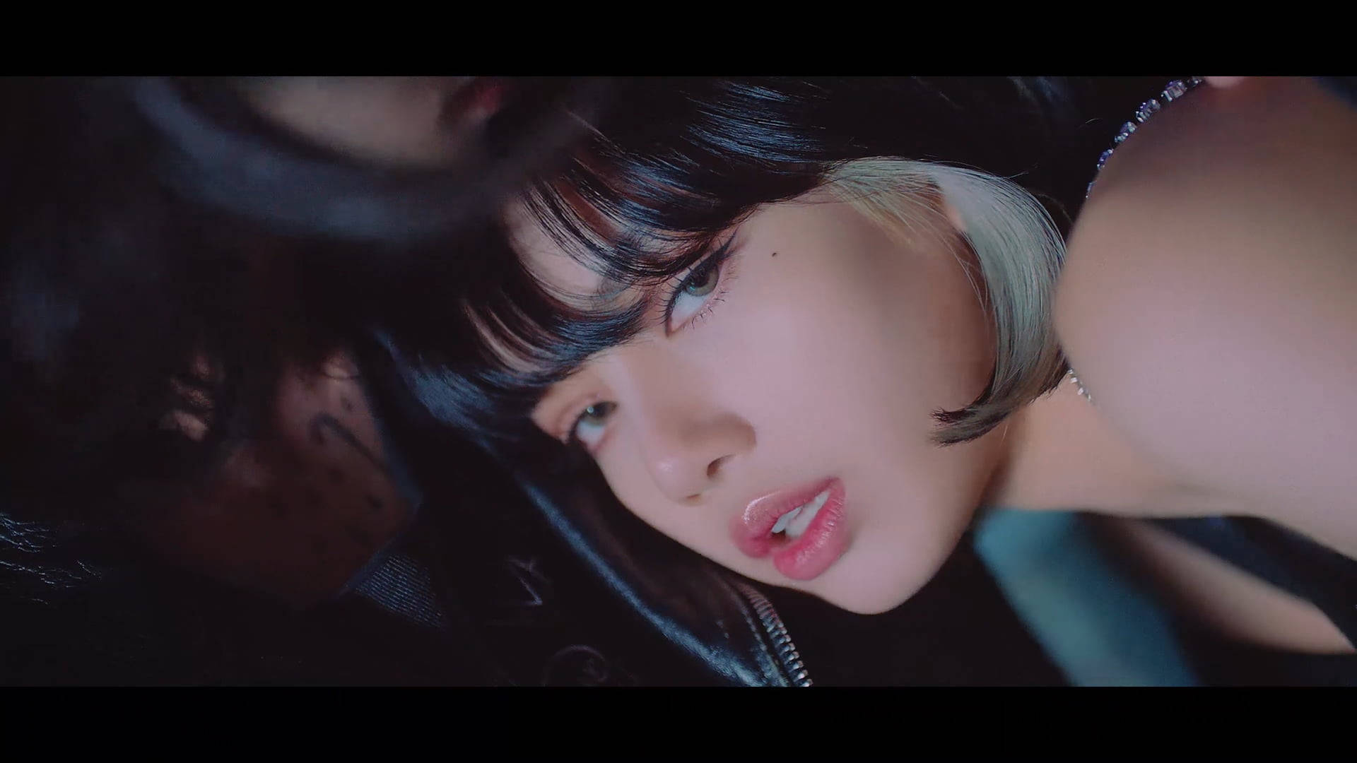 BLACKPINK 成員 Lisa 頭髮有碎髮電腦桌面壁紙 壁紙 — 一個特寫鏡頭，一位深色頭髮帶有銀色挑染的女性，在憂鬱的藍色燈光下以銳利的眼神向上看。