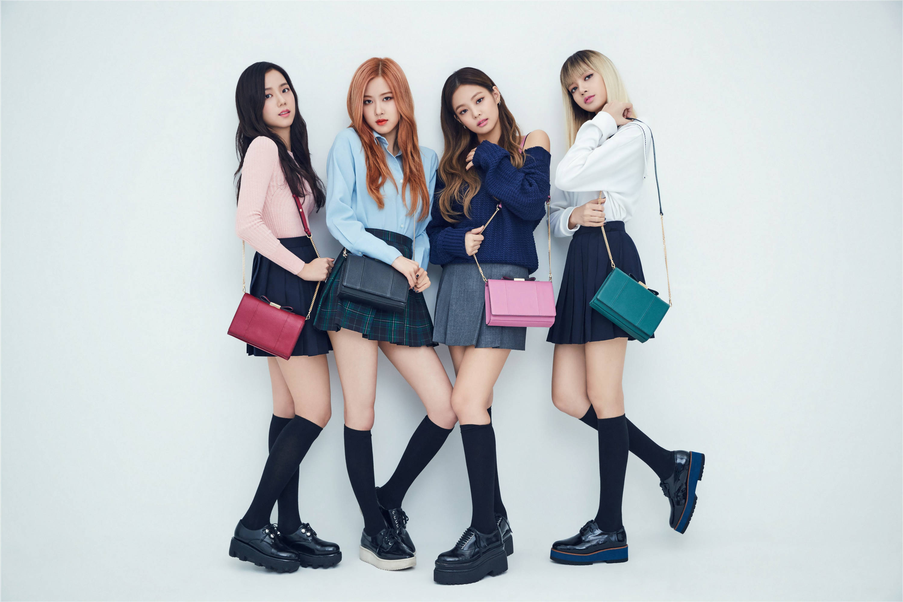 BLACKPINK 搭配彩色斜背包桌面壁紙 壁紙 — 四位時尚年輕女性穿著協調的校服，在純白背景前自信地擺姿勢，每人手持一個色彩繽紛的手袋。