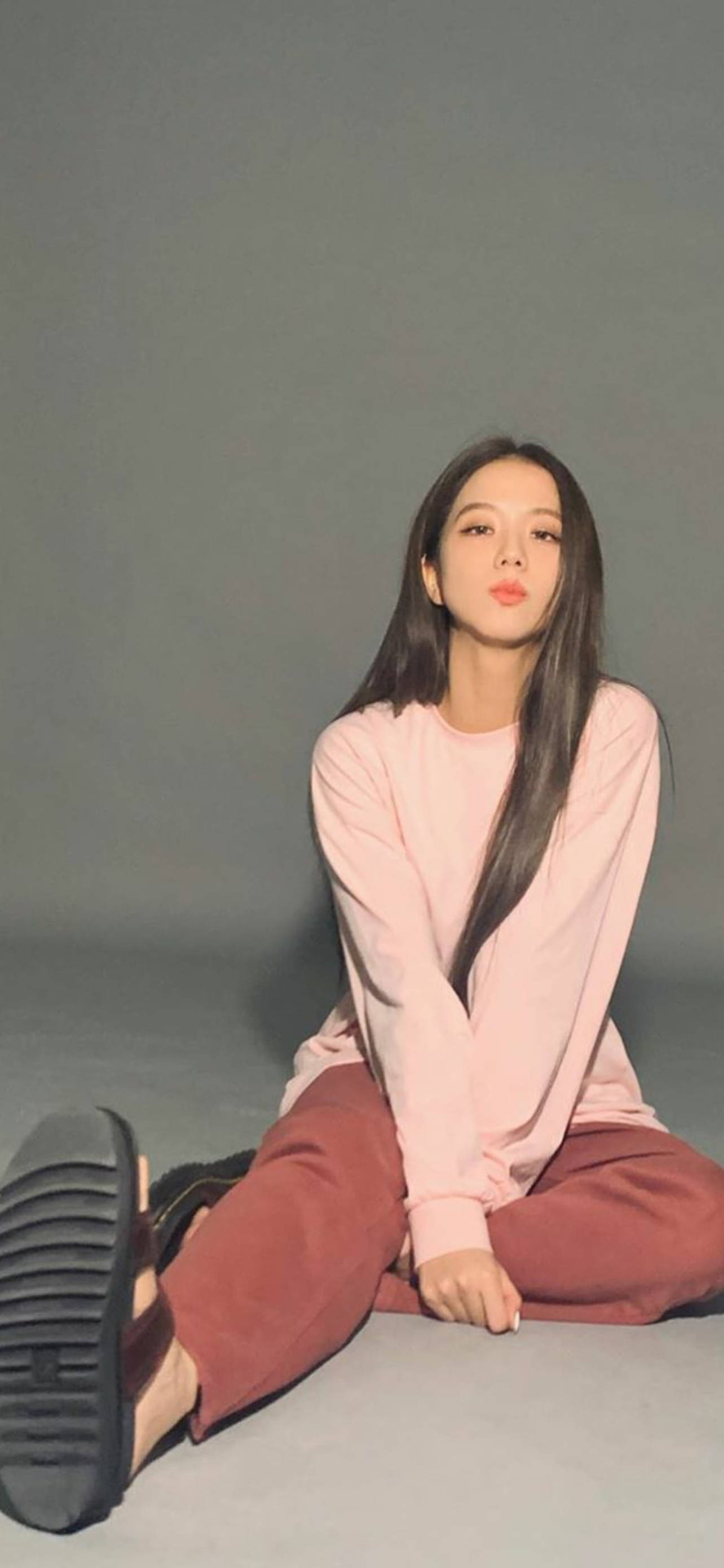 BLACKPINK 智秀休閒風 壁紙 — 一位年輕女性留著深色長髮，盤腿坐在灰色地板上，身穿粉紅色上衣和栗色褲子，直視鏡頭。