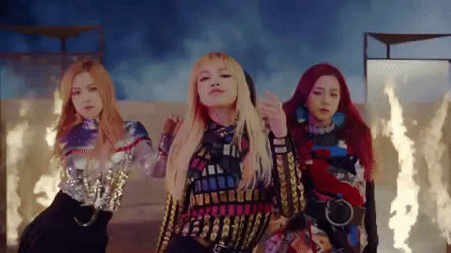 BLACKPINK 梨子身著華麗舞台服裝散發優雅氣質 壁紙 — 三位身穿色彩繽紛未來風格服裝的女性，在超現實沙漠背景前自信擺姿勢，背景有發光的岩石形成。