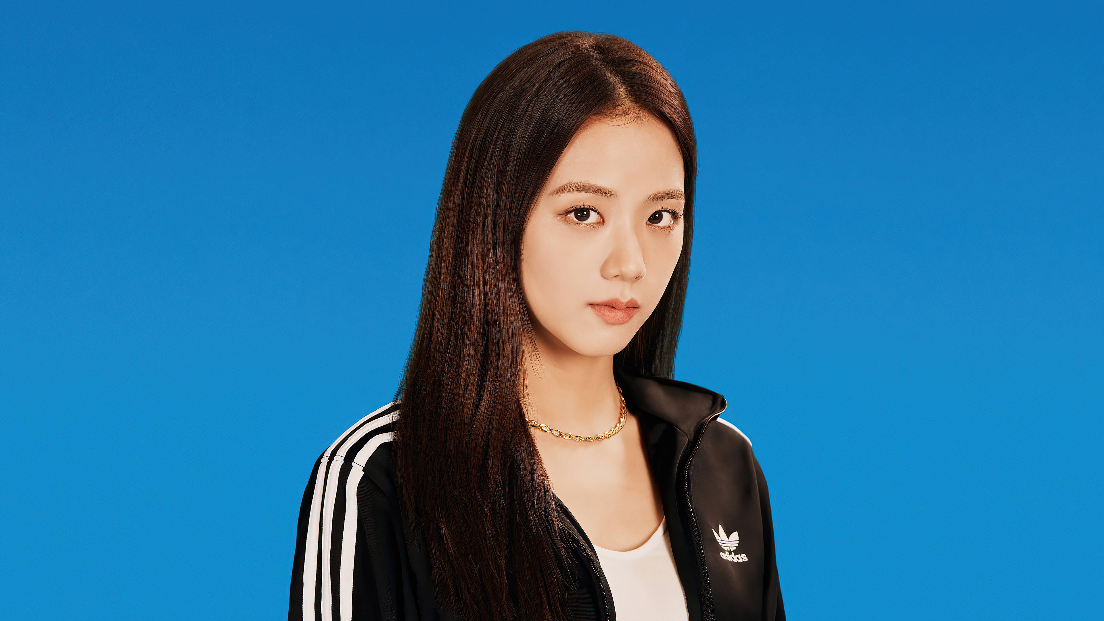 Blackpink 運動風 Jisoo 壁紙 — 一位長黑髮的年輕女性穿著黑色Adidas運動外套，背景為純藍色。