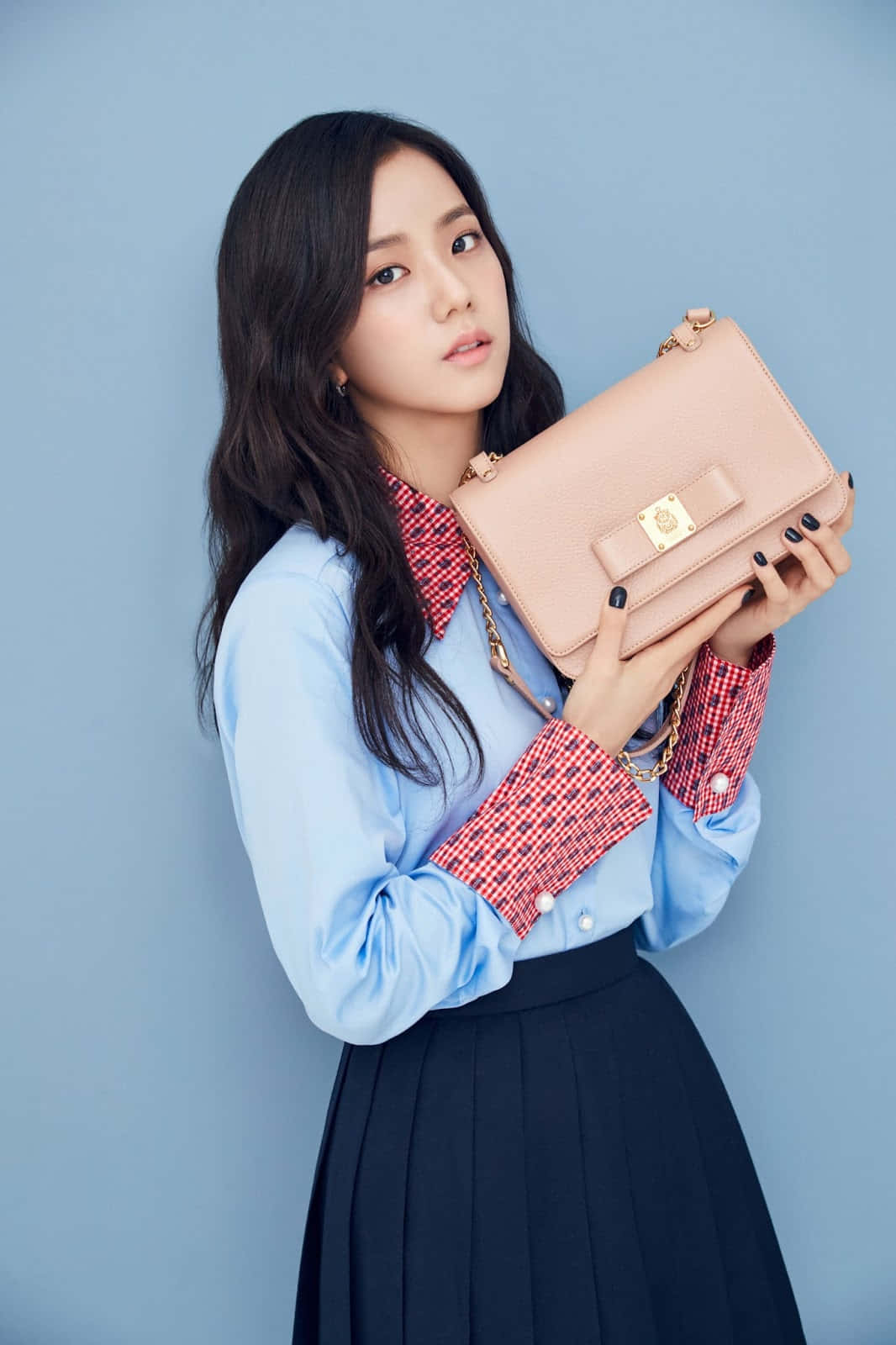 BLACKPINK成員Jisoo以耀眼舞台造型震撼人心 壁紙 — 一位黑髮時尚女性在純藍色攝影棚背景前拿著一個淡粉紅色手提包。