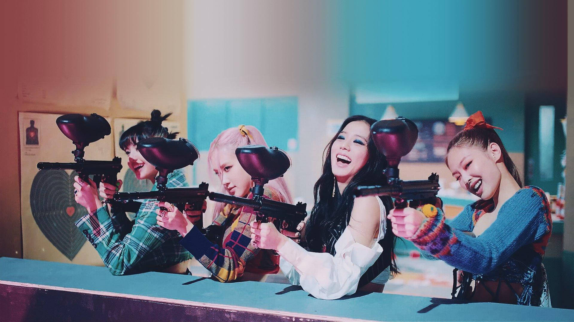 BLACKPINK金珍妮槍擊姿勢 壁紙 — 四位年輕女性在光線明亮的室內競技場中，從障礙物後面笑著瞄準彩彈槍。