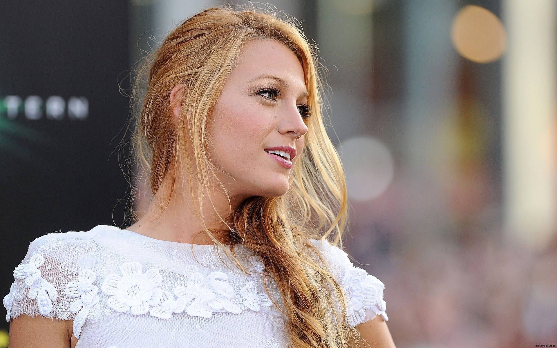 Blake Lively 穿白色襯衫 壁紙 — 金髮女子身穿白色蕾絲連衣裙，在模糊背景中溫柔微笑的特寫。