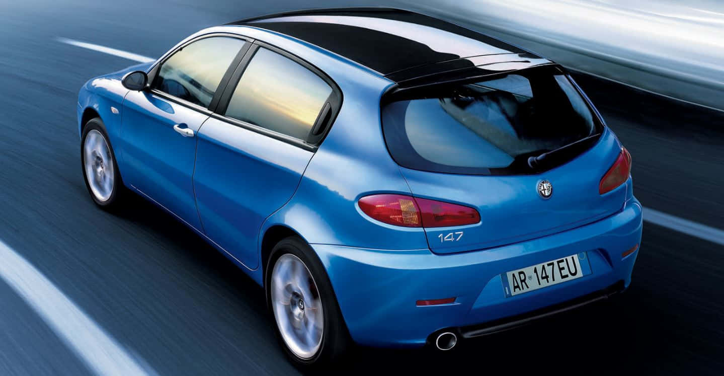 Alfa Romeo 147 桌布 壁紙 — 一輛充滿活力的藍色愛快羅密歐147掀背車在模糊的高速公路上疾馳，運動條紋強調了速度。