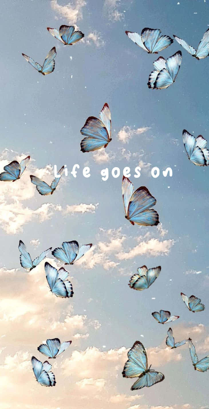  壁紙 — 藍色蝴蝶在柔和天空與縷縷雲彩間優雅飛舞，並帶有「life goes on」字句。
