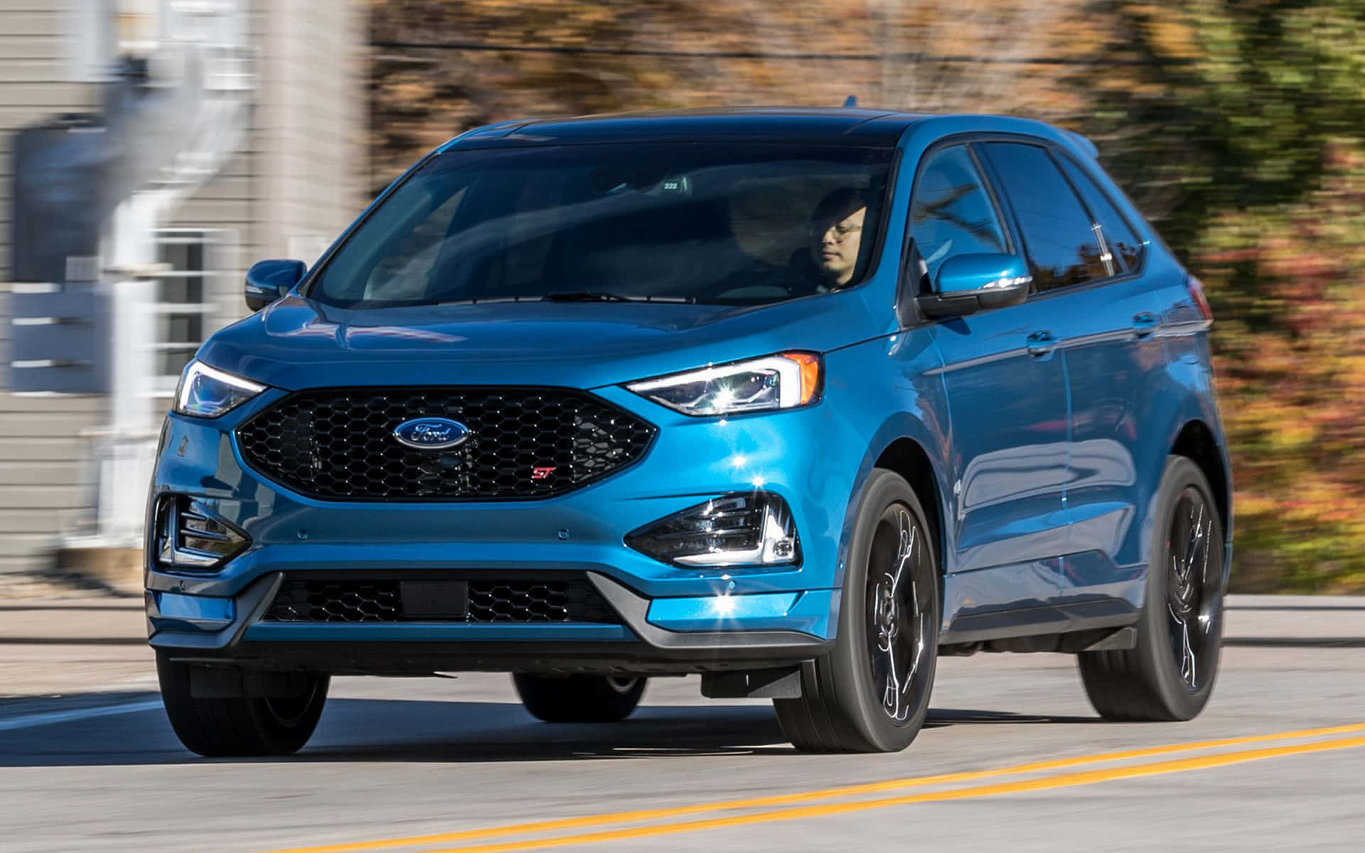 Ford Edge 桌布 壁紙 — 一輛充滿活力的藍色福特 Edge ST SUV 在郊區街道上飛馳，背景中的秋葉模糊不清。