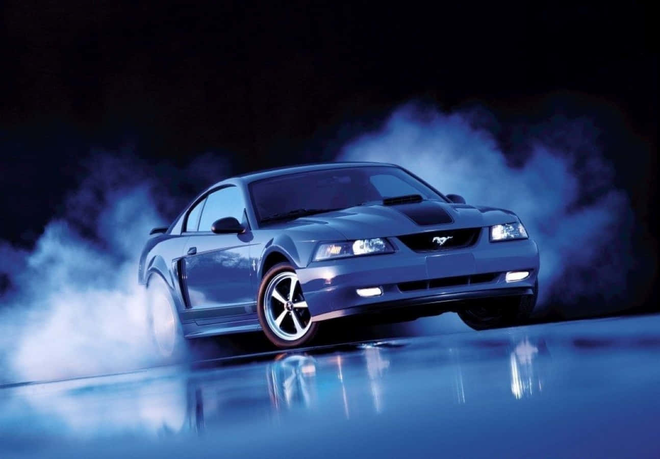 Ford Mustang Mach 1 桌布 壁紙 — 一輛時尚的藍色福特野馬在戲劇性燈光下，在反光的濕滑路面上穿過發光的藍色煙霧漂移。