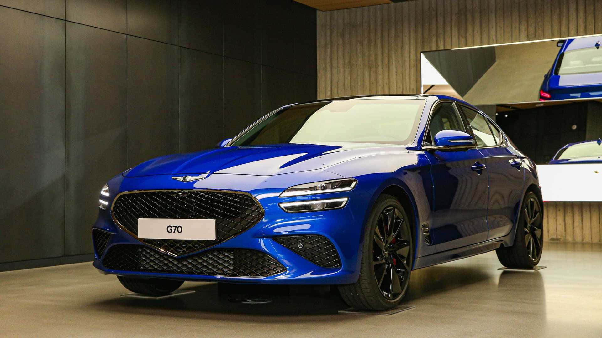 Genesis G70 桌布 壁紙 — 一輛閃亮的藍色Genesis G70運動型轎車在現代展廳中展示，展廳有深色牆壁和反光地板。