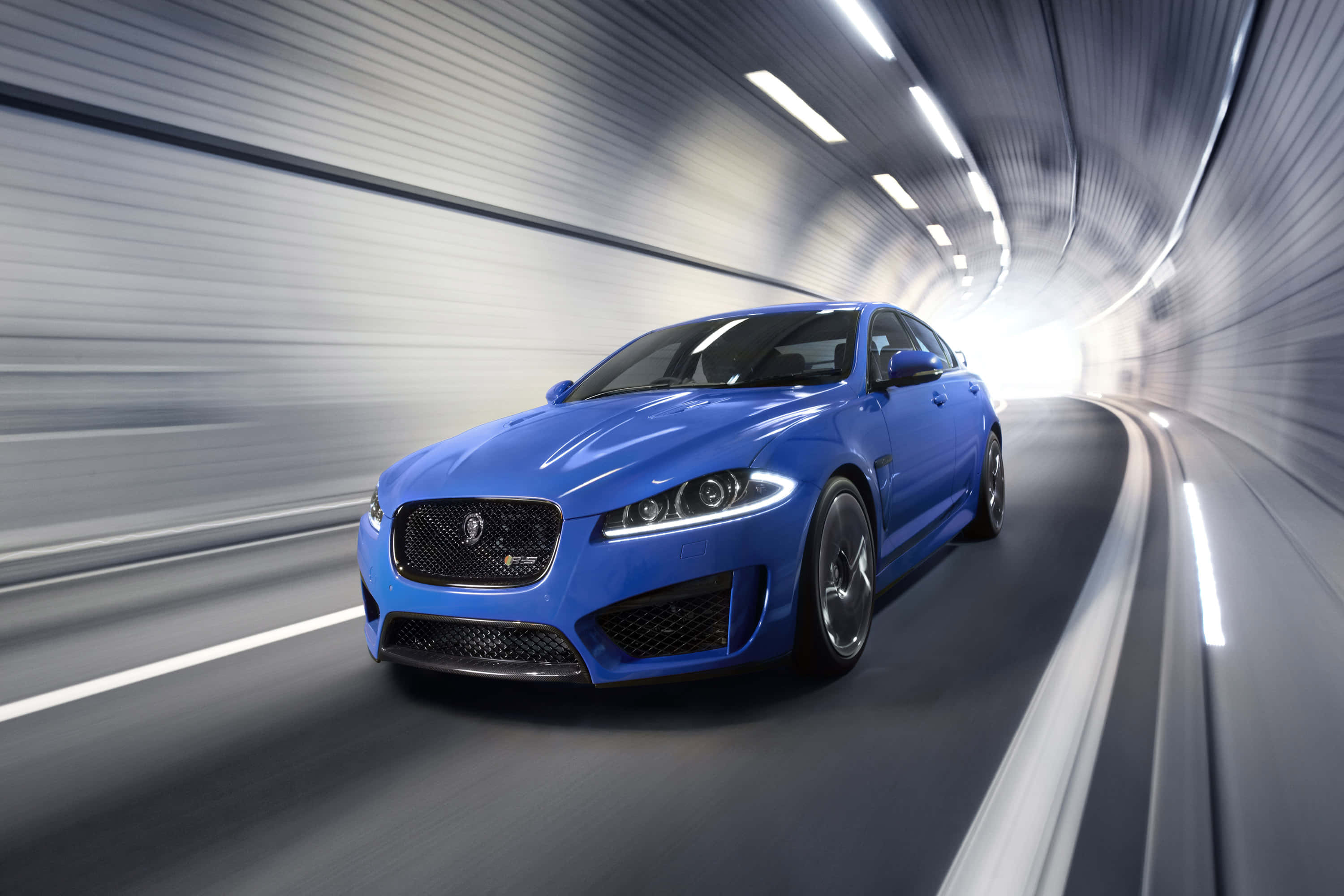 Jaguar Xfr 桌布 壁紙 — 一輛充滿活力的藍色Jaguar跑車在時尚的隧道中疾馳，動態模糊強調了速度。