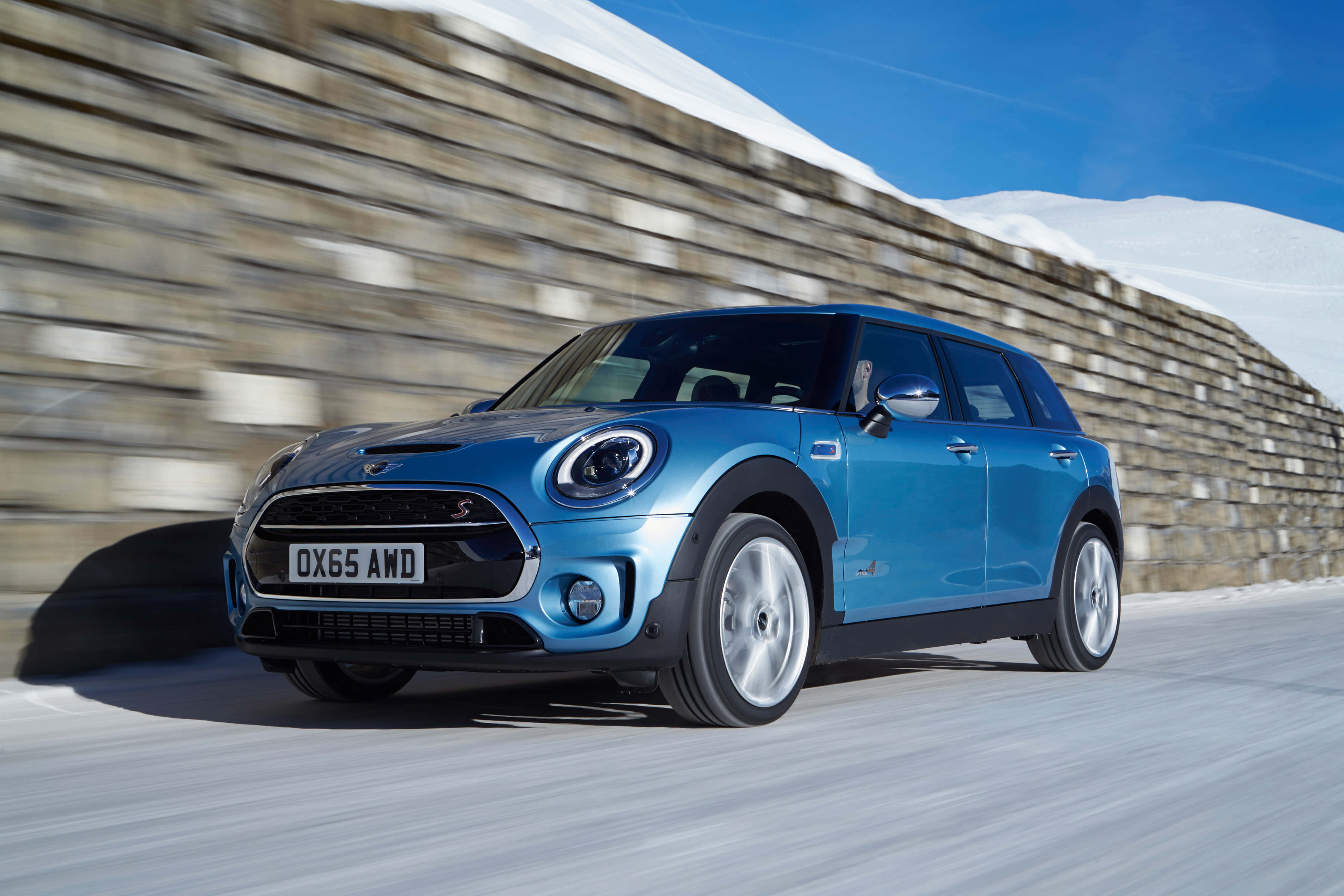 Mini Cooper S Clubman All4 桌布 壁紙 — 一輛充滿活力的藍色MINI Countryman在晴朗的藍天下，沿著石牆旁的雪路疾馳。
