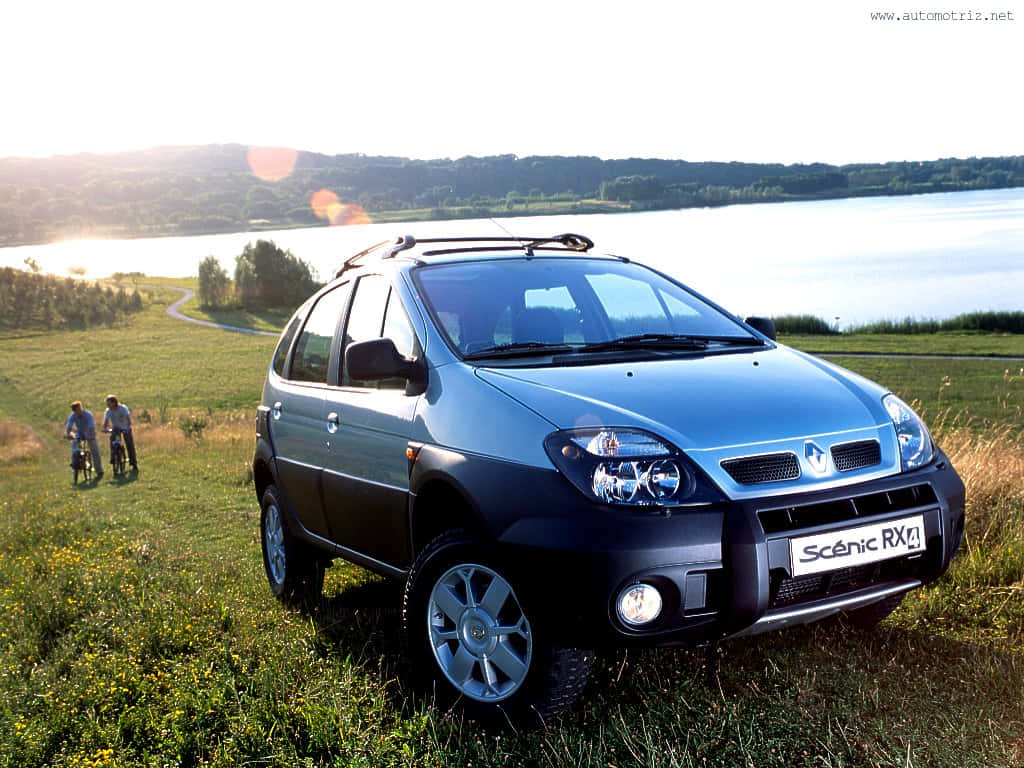 Renault Scenic 桌布 壁紙 — 一輛藍色雷諾 Scenic RX4 SUV 停在湖邊草地上，背景有兩位騎單車人士，在溫暖的日落光線下。