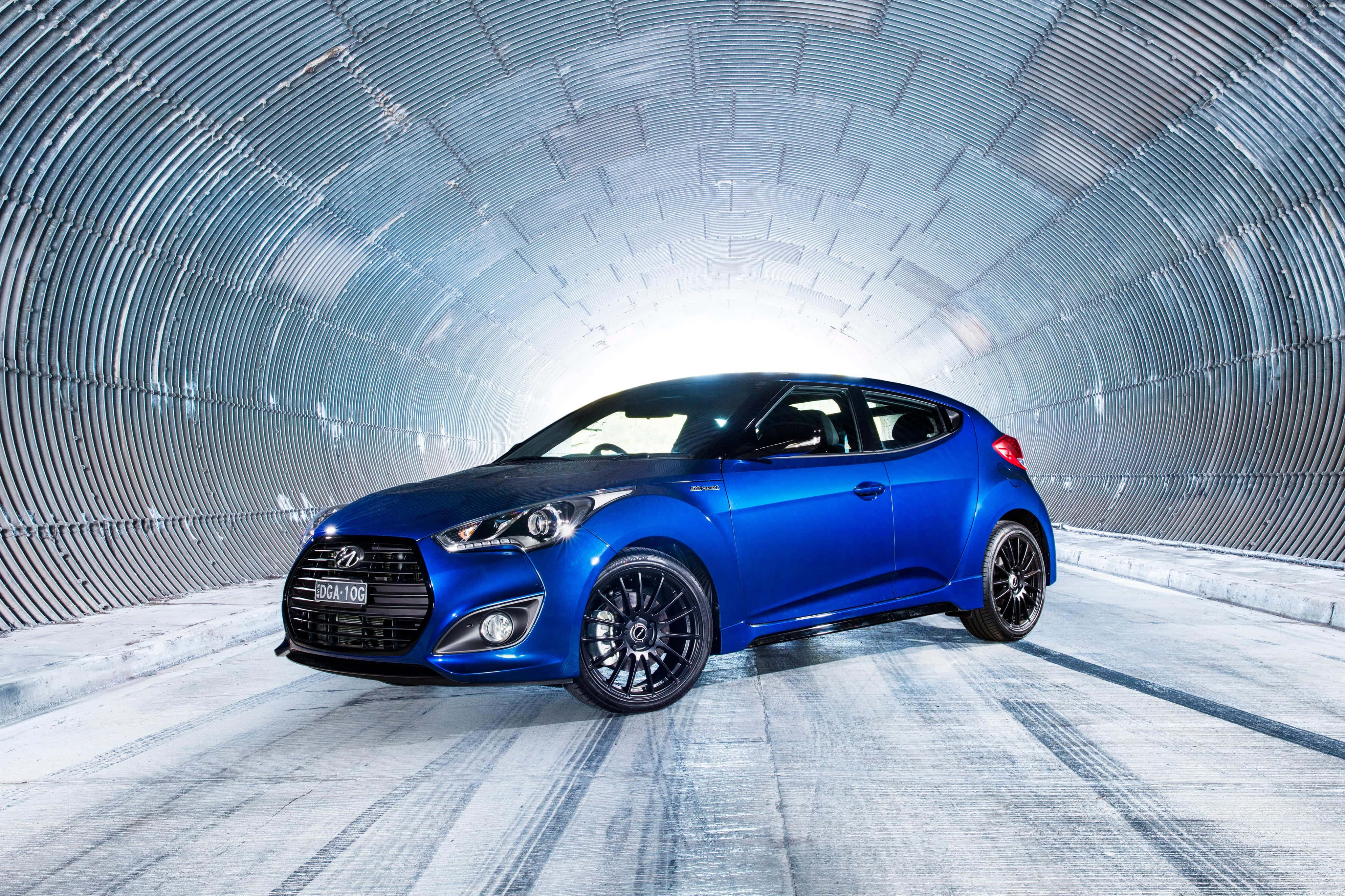 Hyundai Veloster 桌布 壁紙 — 一輛鮮藍色的現代Veloster跑車在金屬波紋隧道內明亮燈光下閃閃發光。