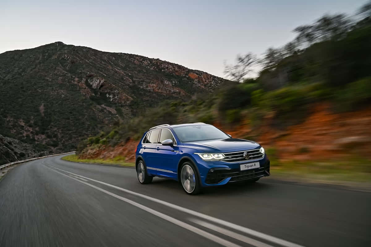 Volkswagen Tiguan 桌布 壁紙 — 一輛鮮藍色的Volkswagen Tiguan R在蜿蜒的山路上疾馳，背景是模糊的綠樹和岩石地形。
