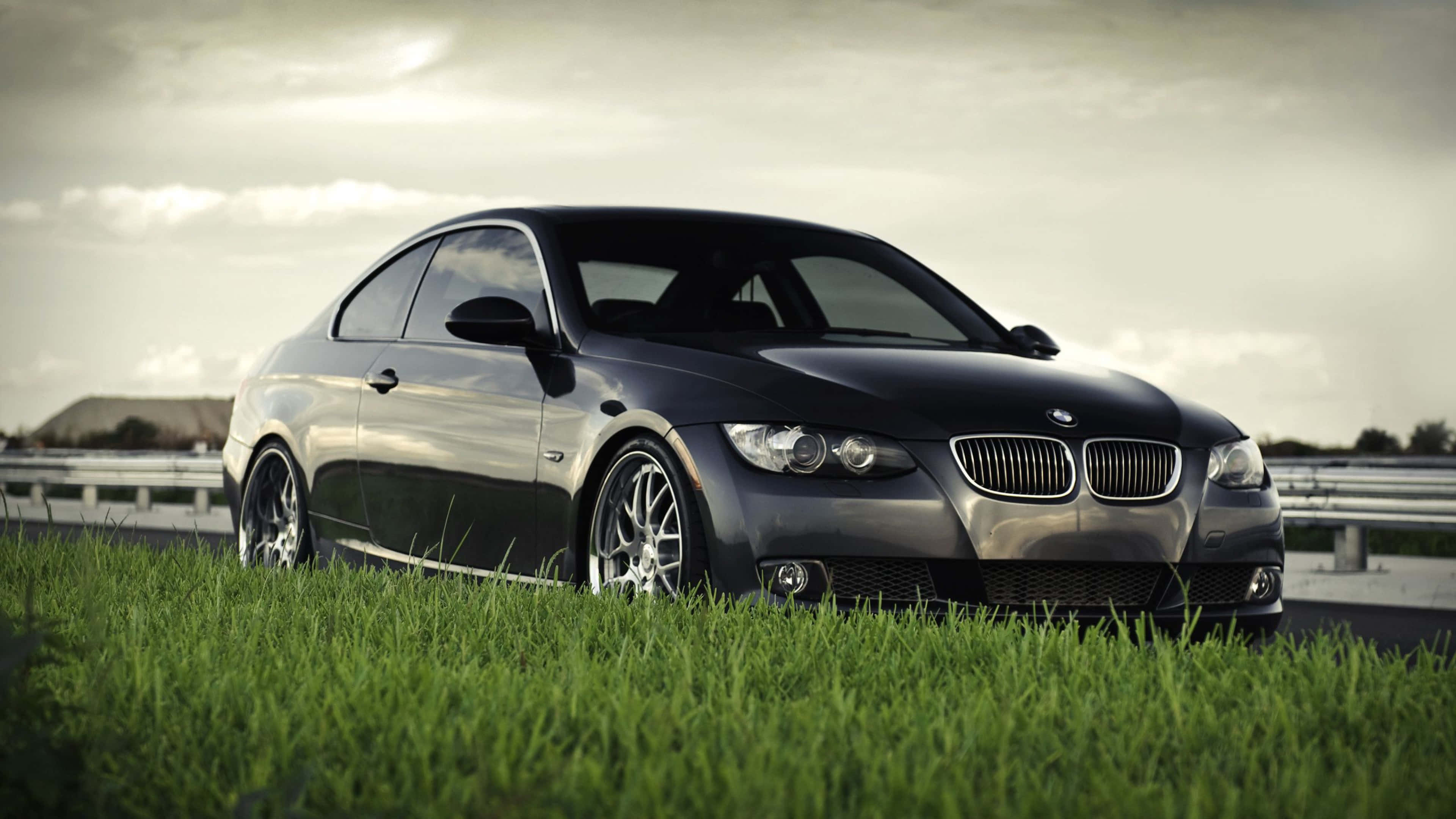 迷人藍色 BMW 328 壁紙 — 一輛時尚的黑色寶馬雙門轎跑車停在高速公路旁的草地上，天空多雲。