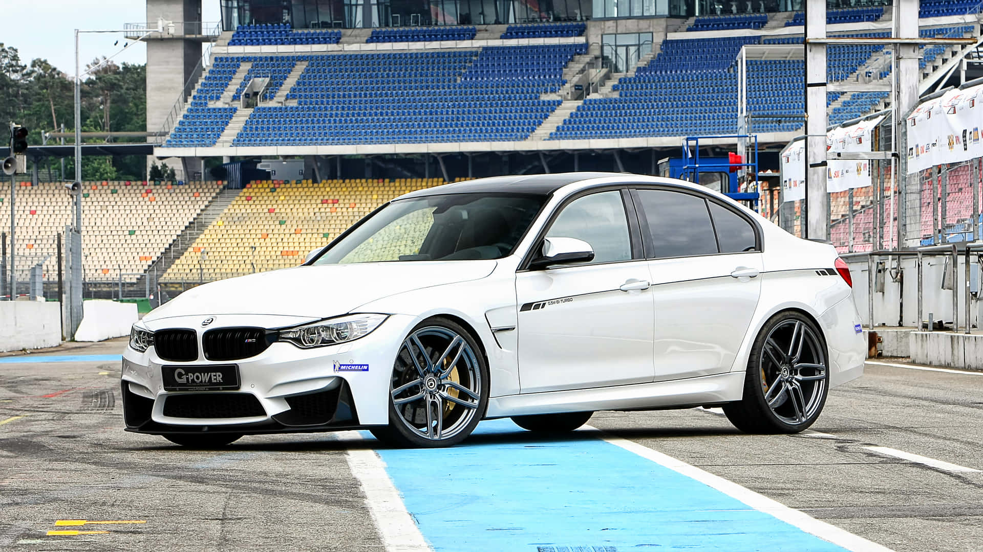 白色BMW M3賽車在賽道上，後面有看台