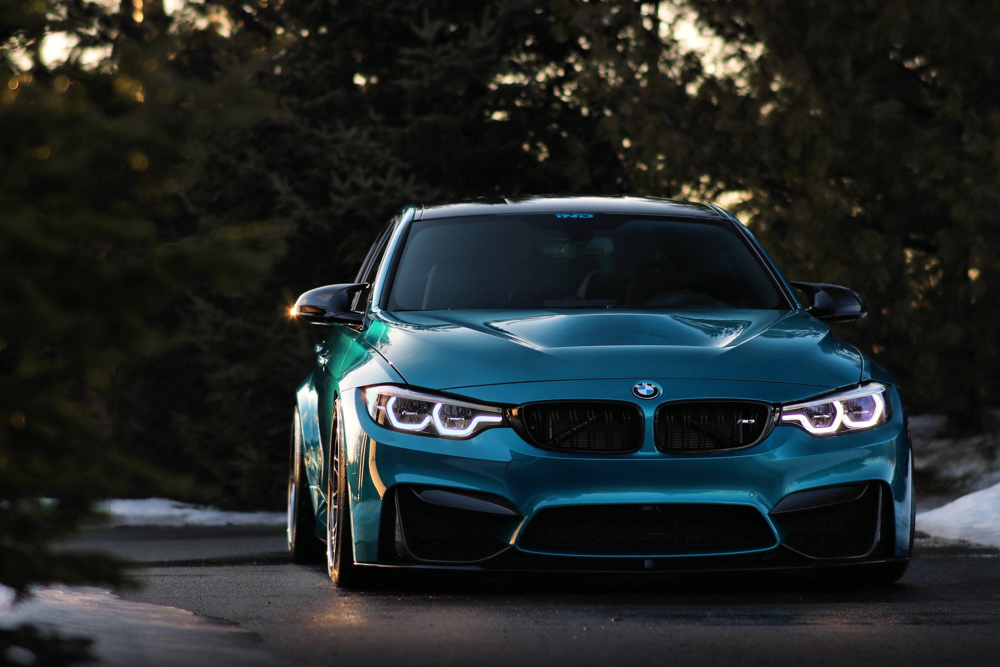 青綠色 BMW 電腦壁紙 壁紙 — 一輛青綠色的BMW M4跑車在白雪覆蓋的森林道路上，在金黃色的夕陽光下閃閃發光。