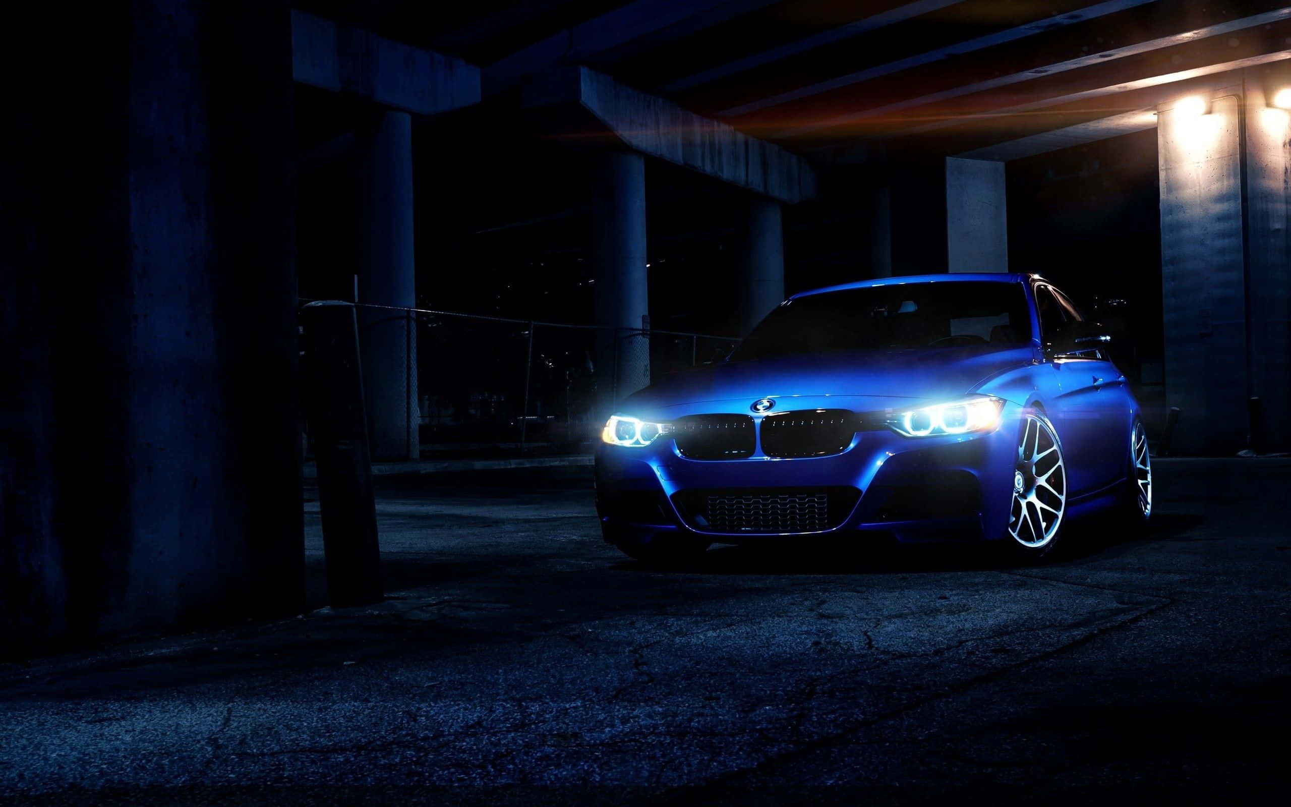 BMW 335i金屬藍色平板壁紙 壁紙 — 一輛發光的藍色跑車在夜間亮著明亮的前燈停放在黑暗的混凝土天橋下。