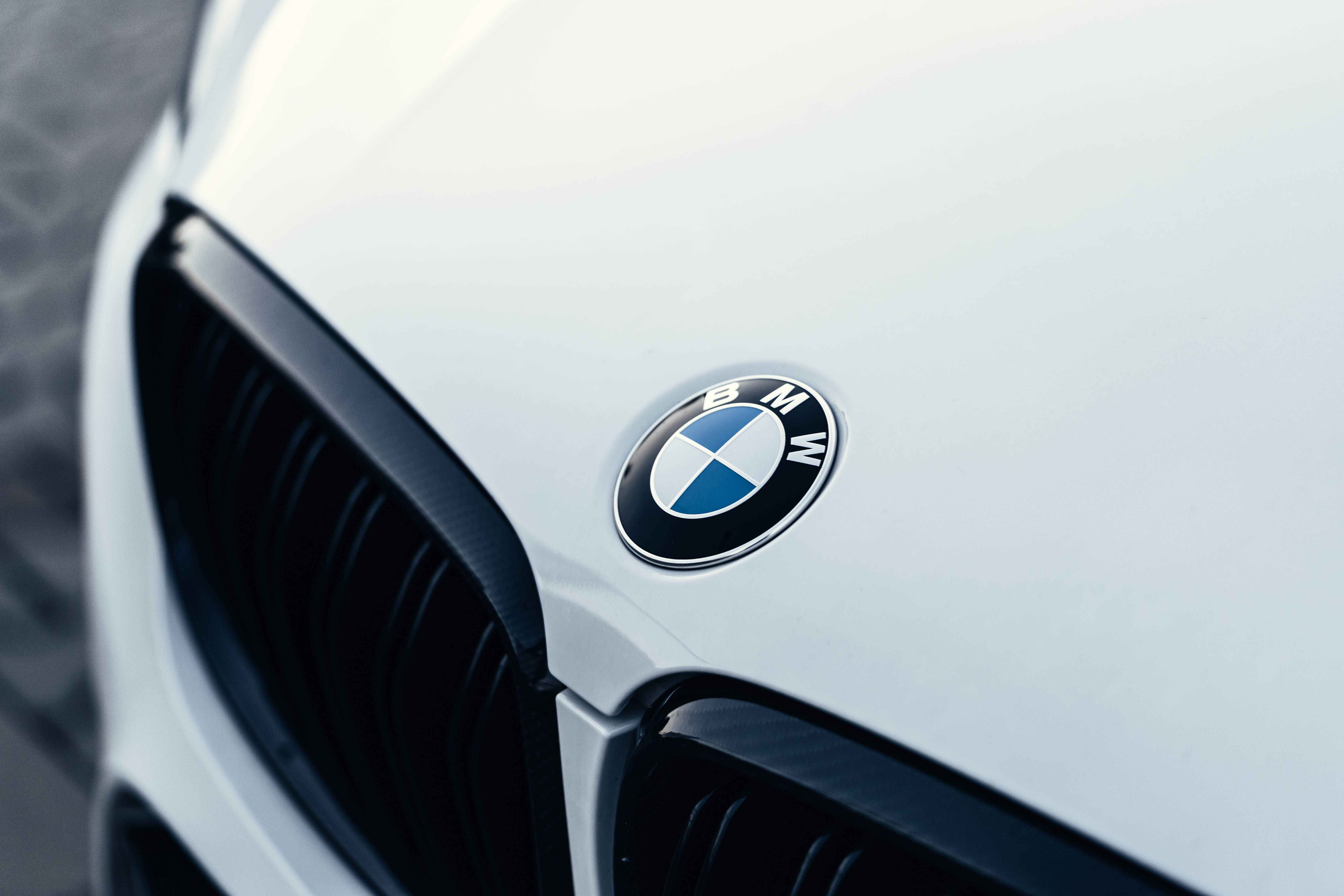 白色豪華跑車引擎蓋配BMW標誌 壁紙 — 白色寶馬汽車引擎蓋的特寫，經典的藍白圓形標誌旁邊是黑色腎形格柵。