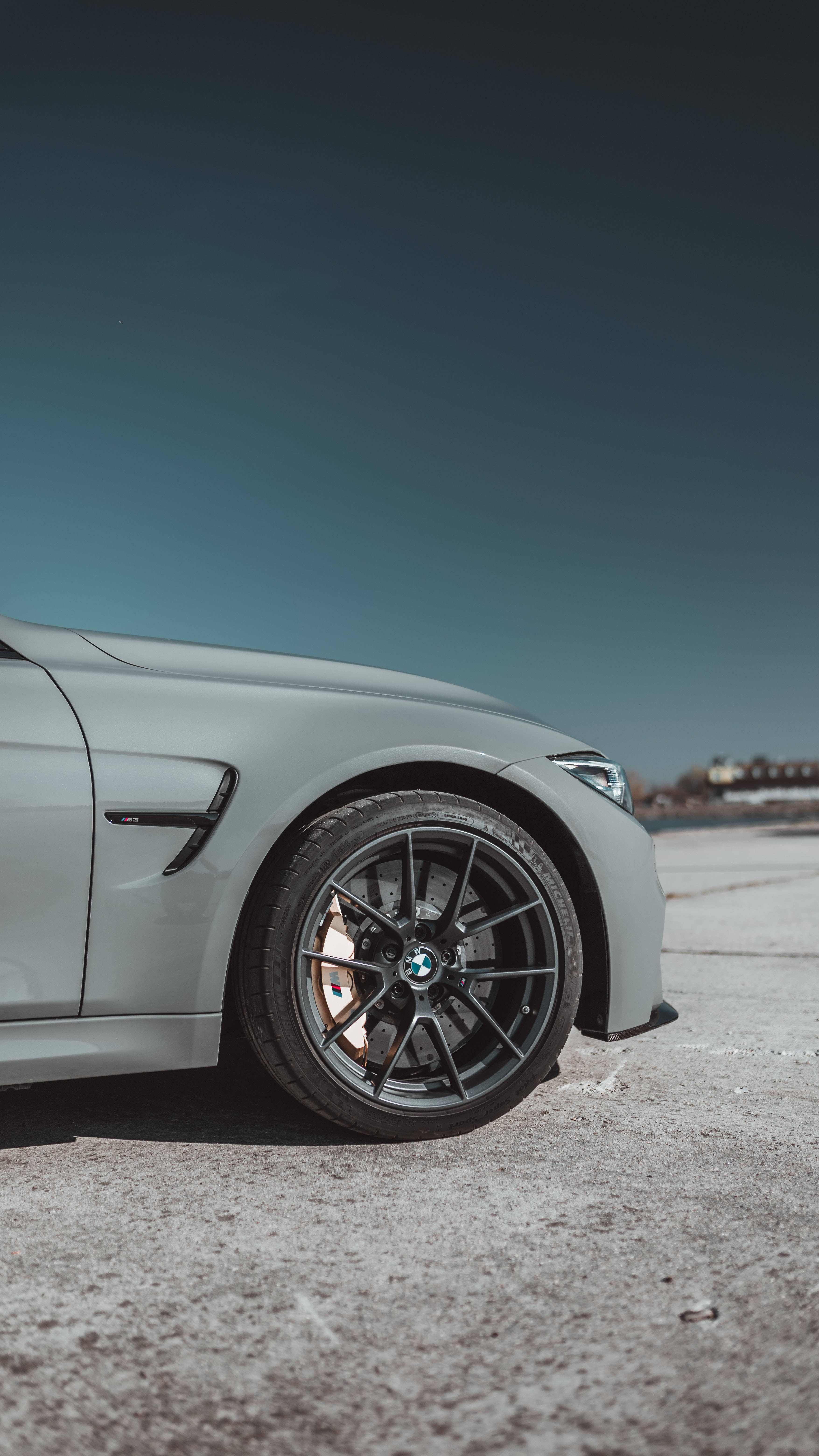 灰色BMW車款的完美視角 壁紙 — 一輛流線型銀色寶馬跑車的前輪和擋泥板在晴朗藍天下於混凝土表面上閃閃發光。