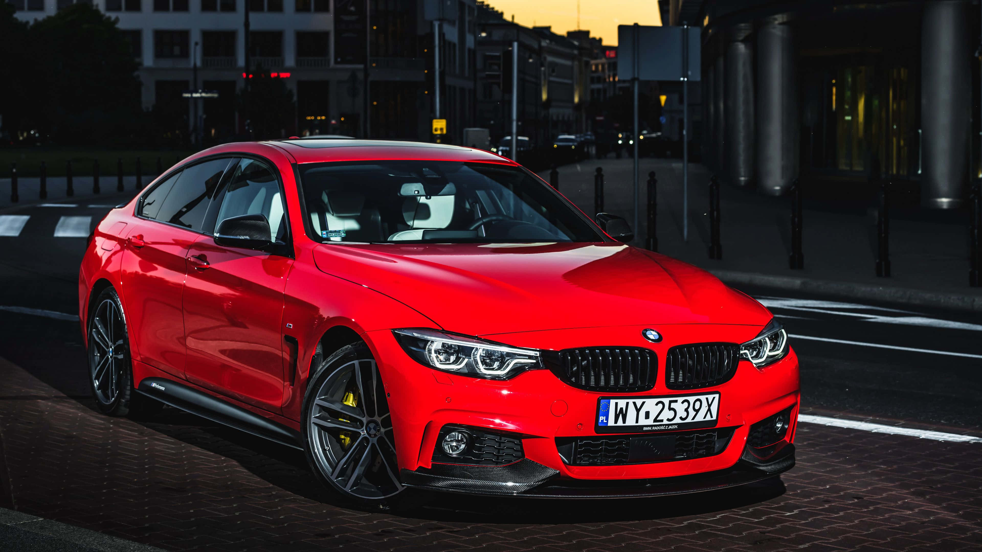 力量與優雅的完美結合 —— BMW 440i 壁紙 — 一輛鮮紅色的BMW雙門跑車在金色夕陽下閃耀，背景是模糊的城市建築。